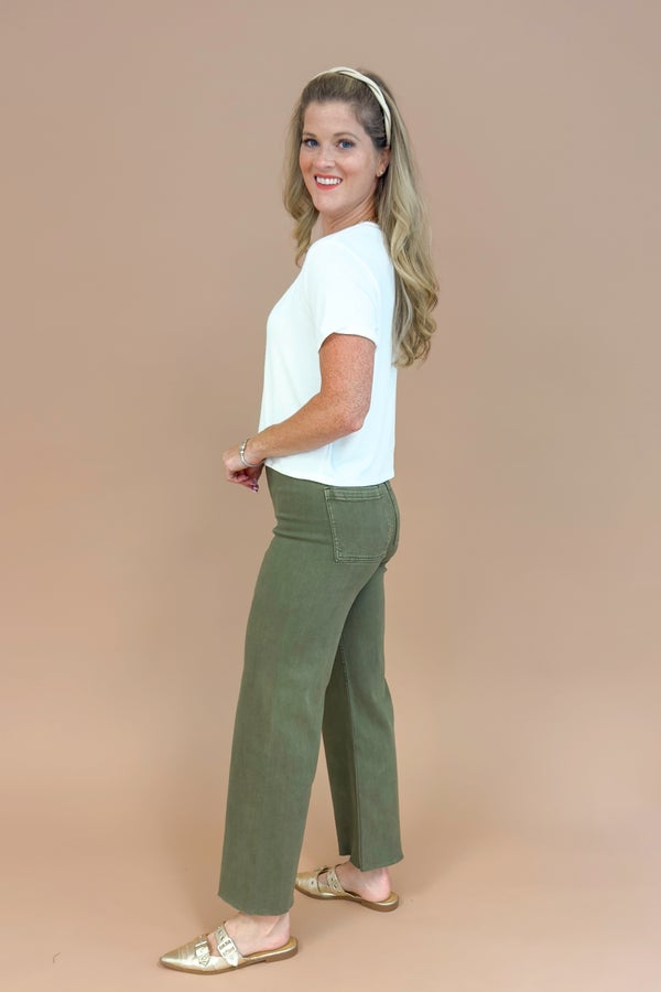 Woman wearing a white top and green pants on a beige background