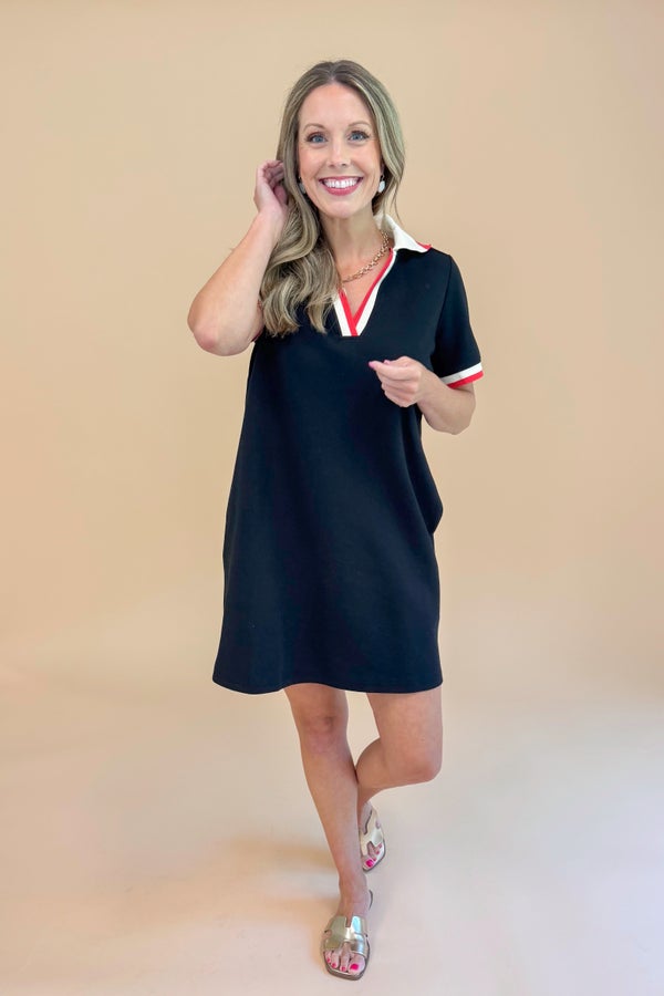 Woman wearing a black dress with a white collar and red trim on a beige background