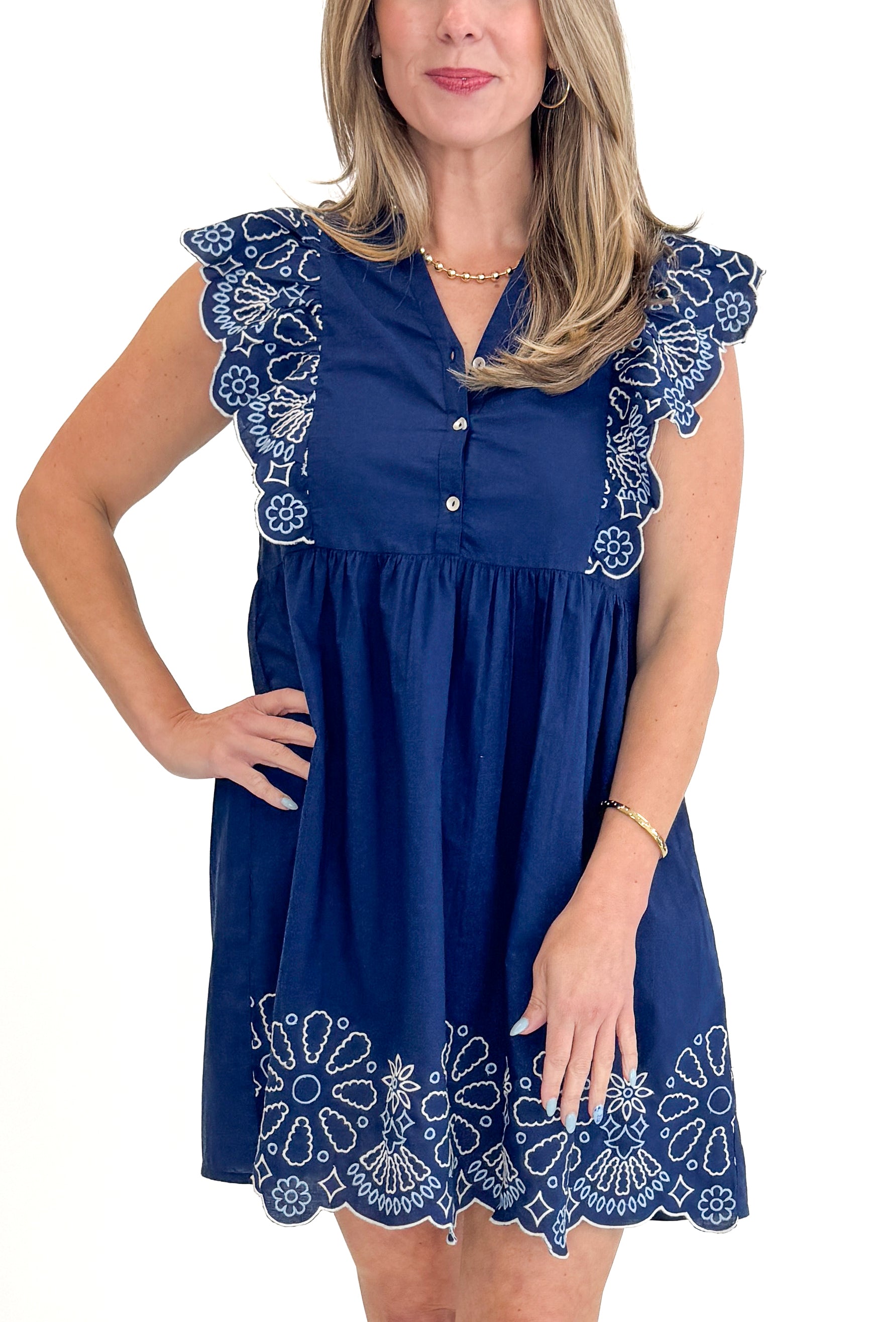 Front detail view of woman wearing Navy Oakes Embroidered Dress by MudPie against white studio background.