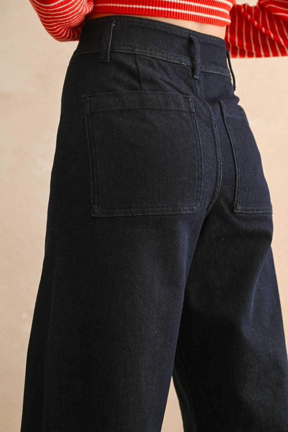 Back view of woman in a studio wearing Dark Indigo Wide Leg Jeans and print top with a tan background.