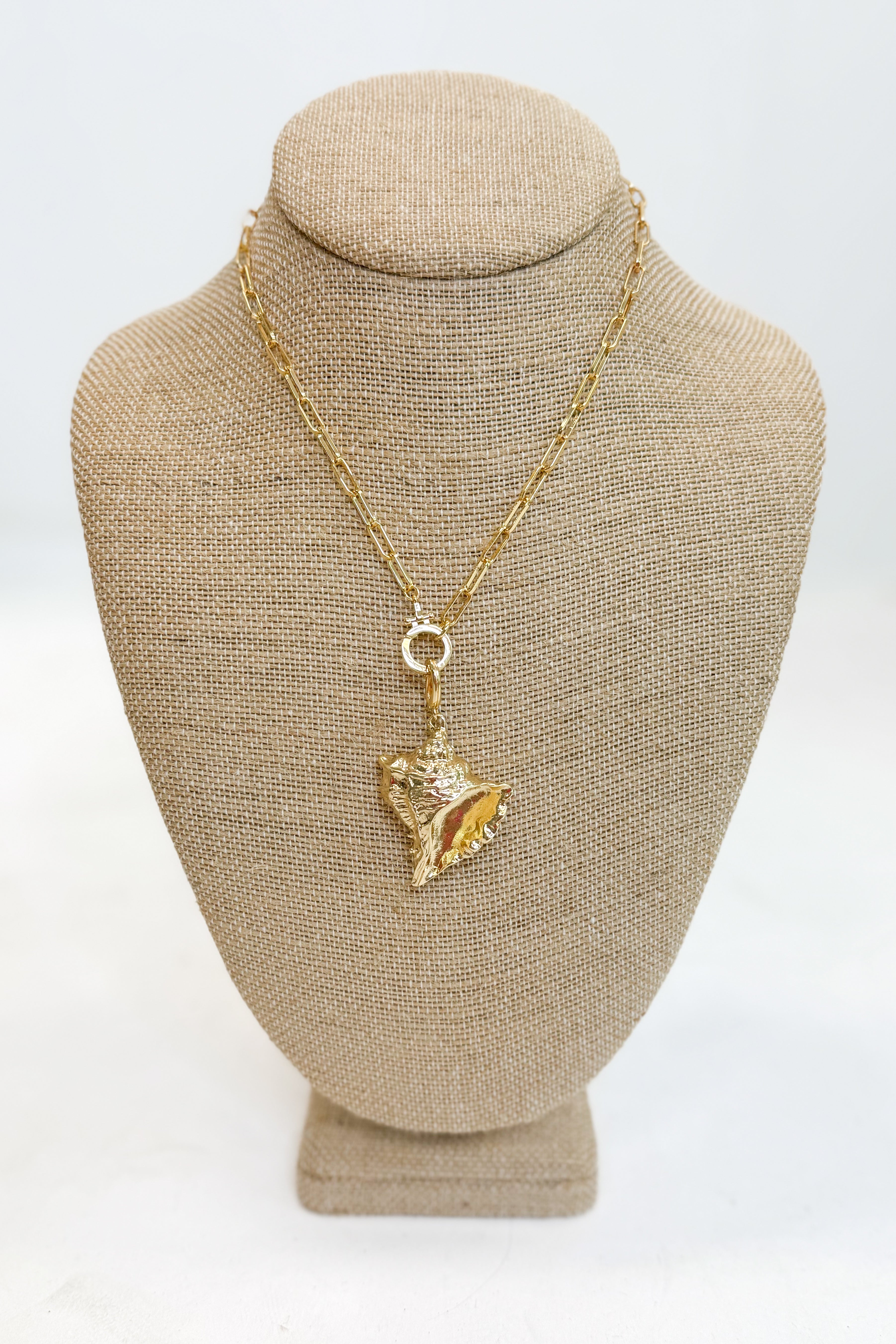 Gold necklace with a pendant on a beige mannequin bust against a white background