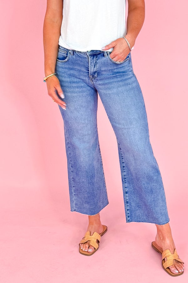 Person wearing blue jeans and a white top on a pink background