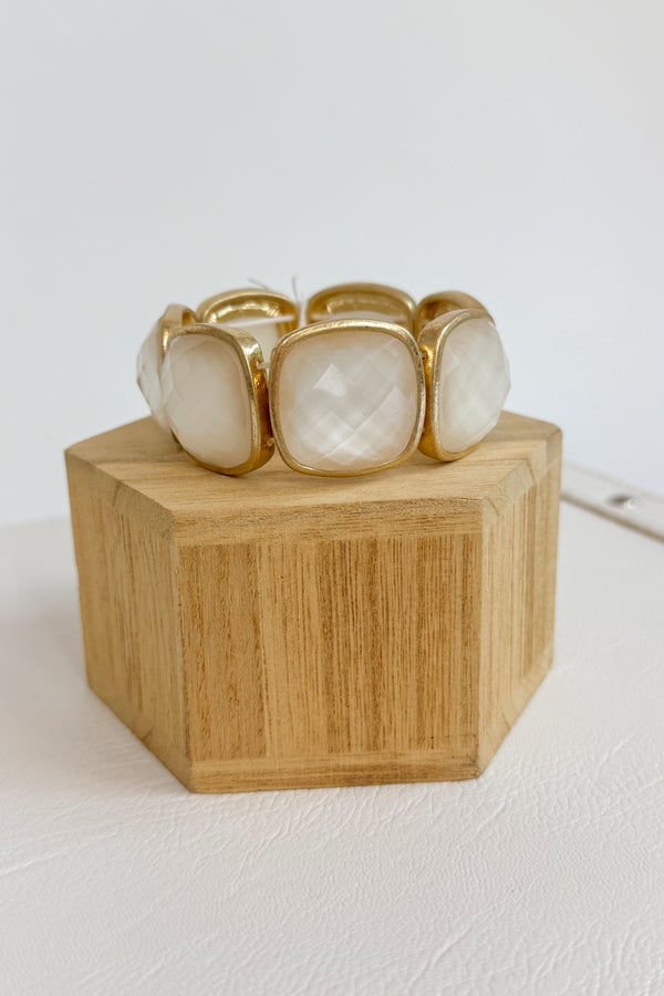 Gold and white stone bracelet on a wooden block against a white background