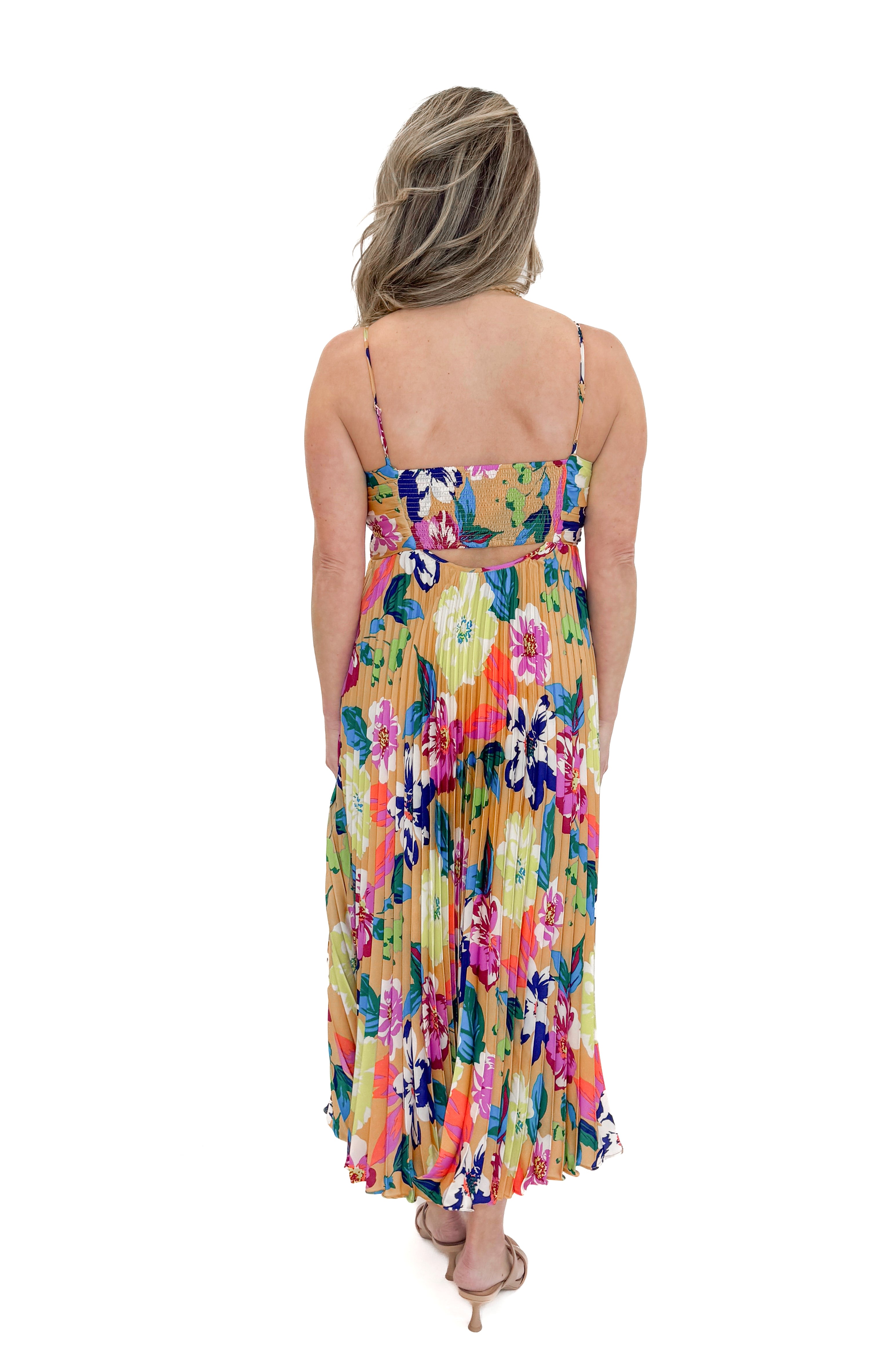 Back view of woman wearing Taupe & Multi Floral Print Pleated Midi Dress by Skies Are Blue against white studio background.