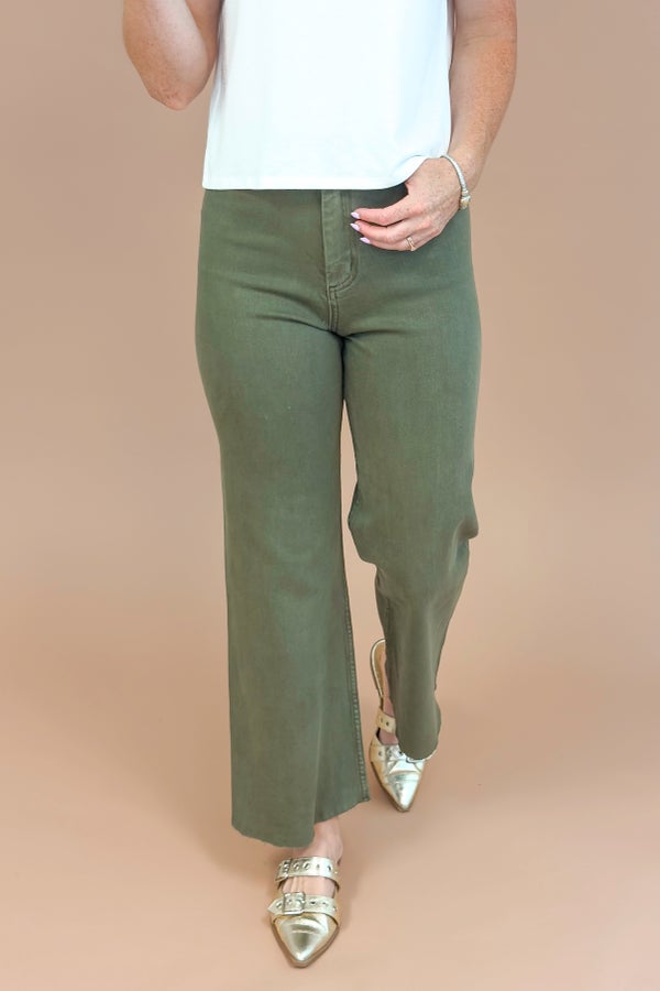 Person wearing green pants and white top on a beige background