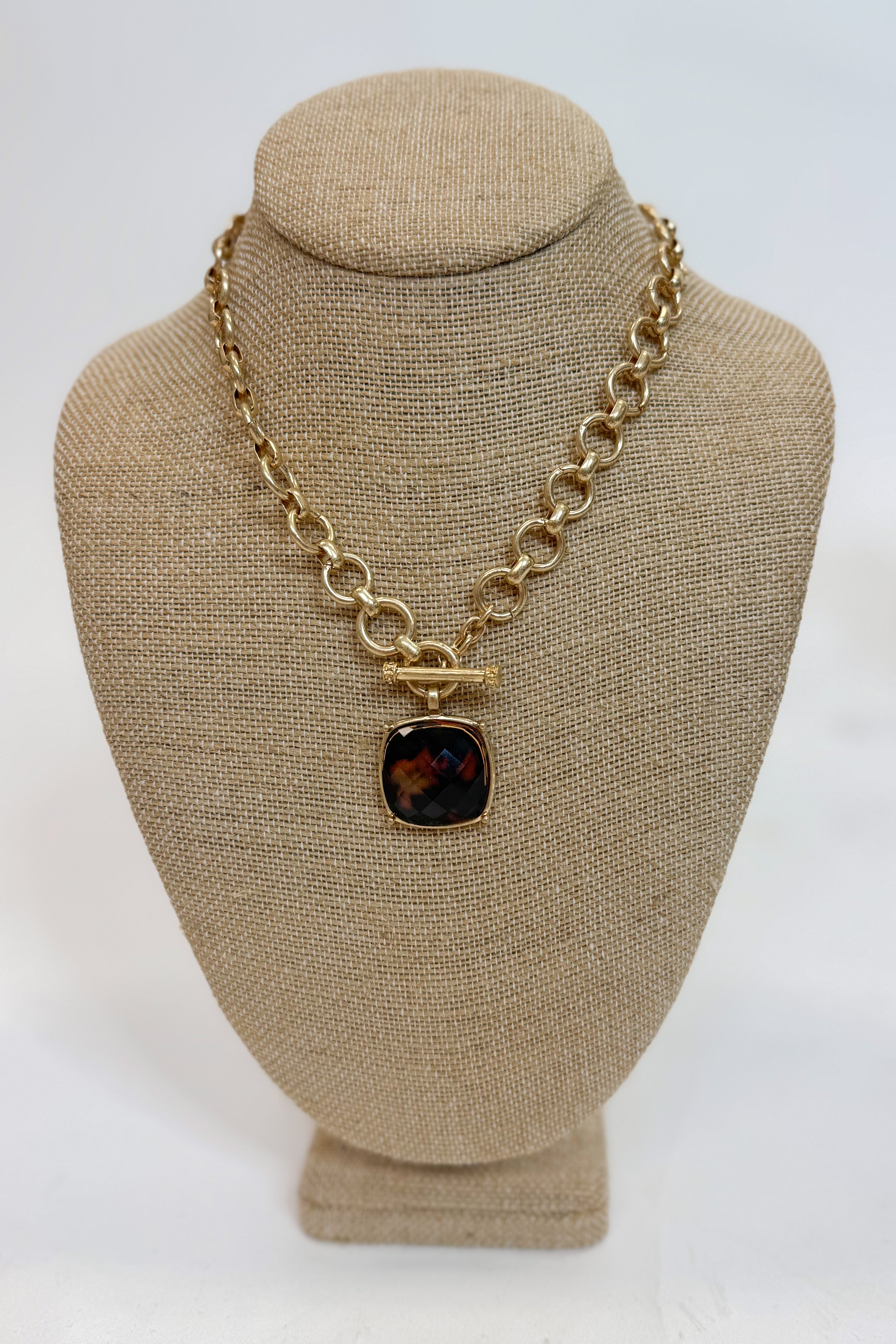 Gold chain necklace with a brown pendant on a beige bust