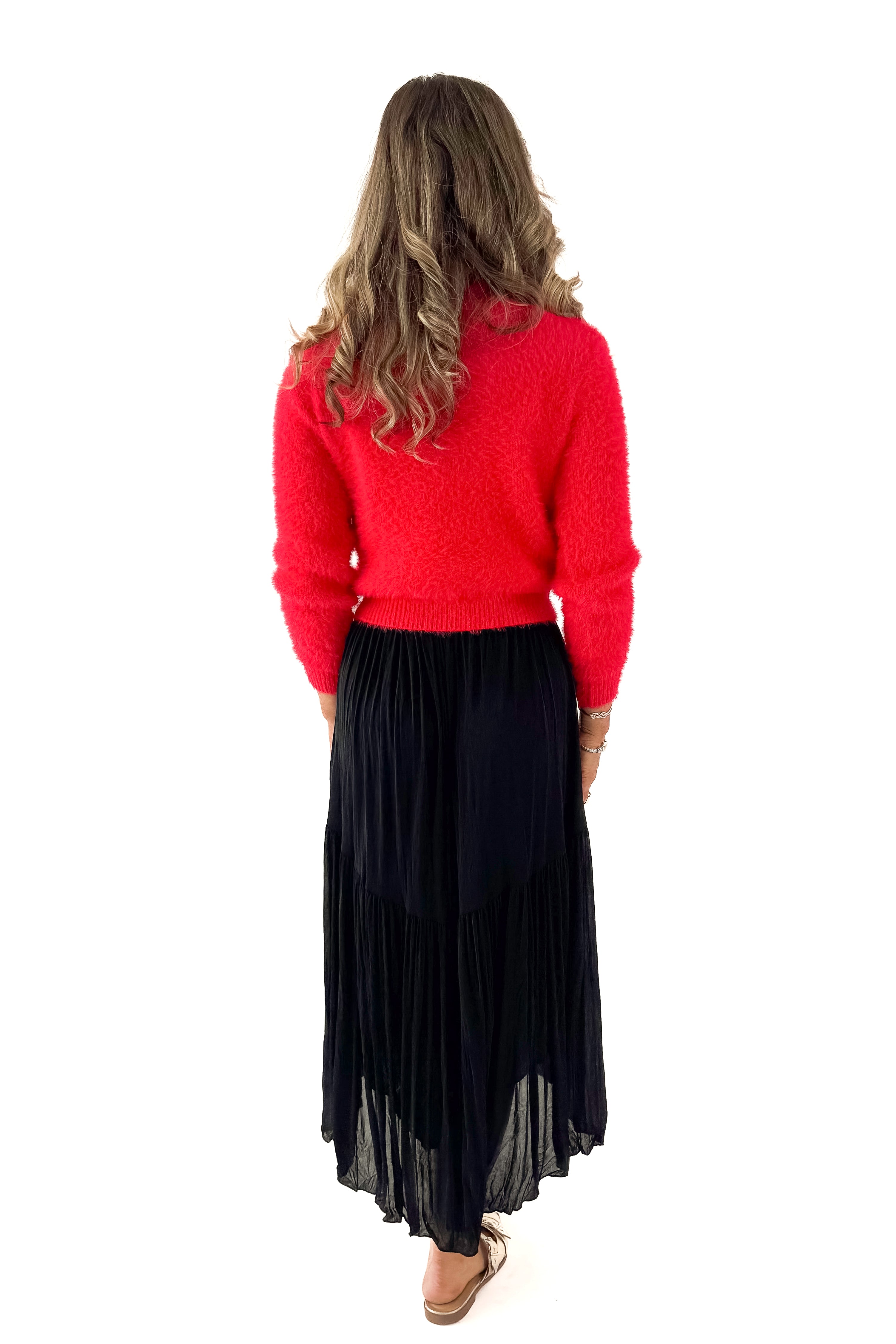 Back view of woman wearing red sweater with black skirt against white studio background.
