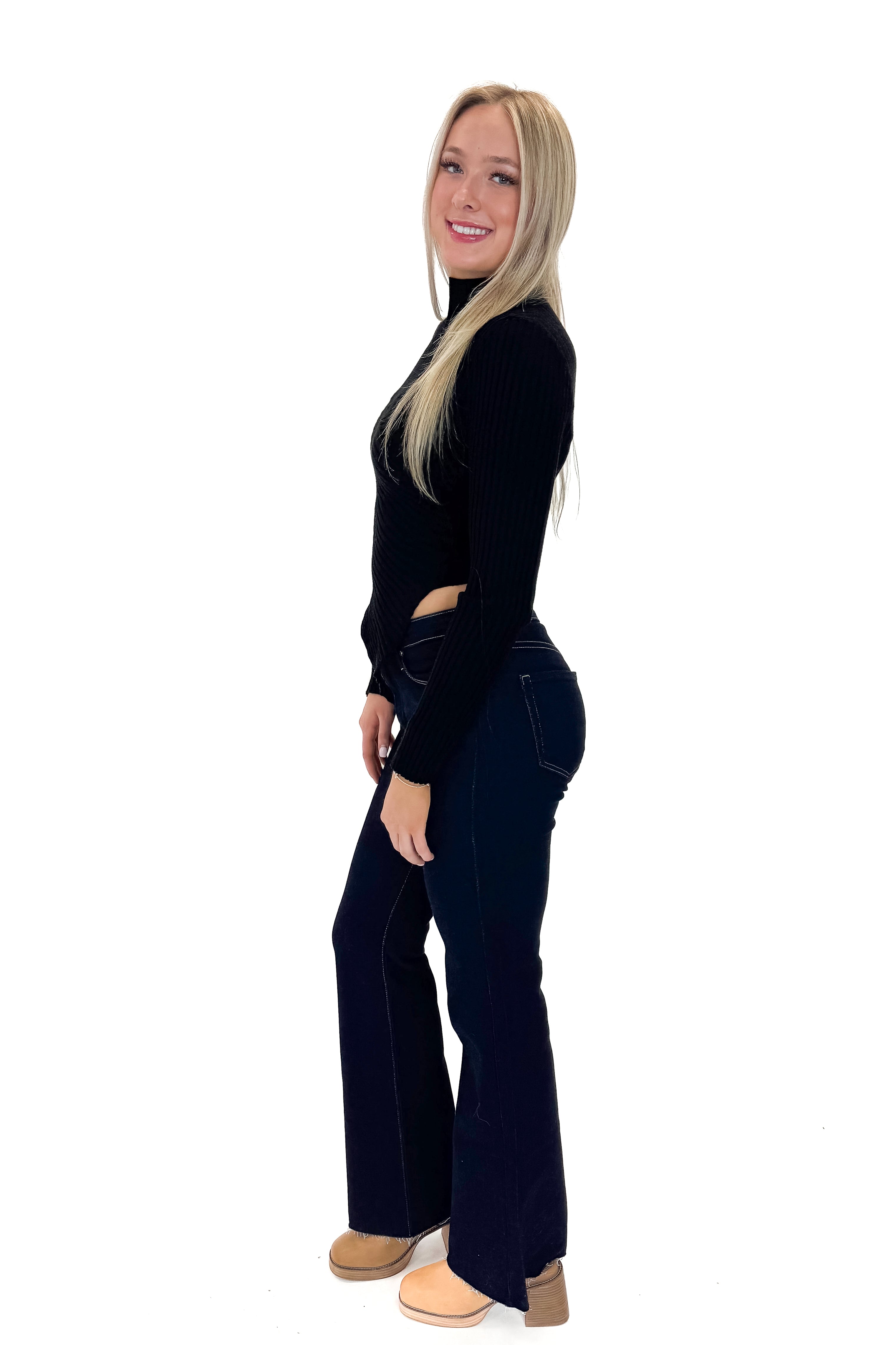 Side view of woman wearing Black Ribbed Asymmetrical Top with jeans against white studio background.