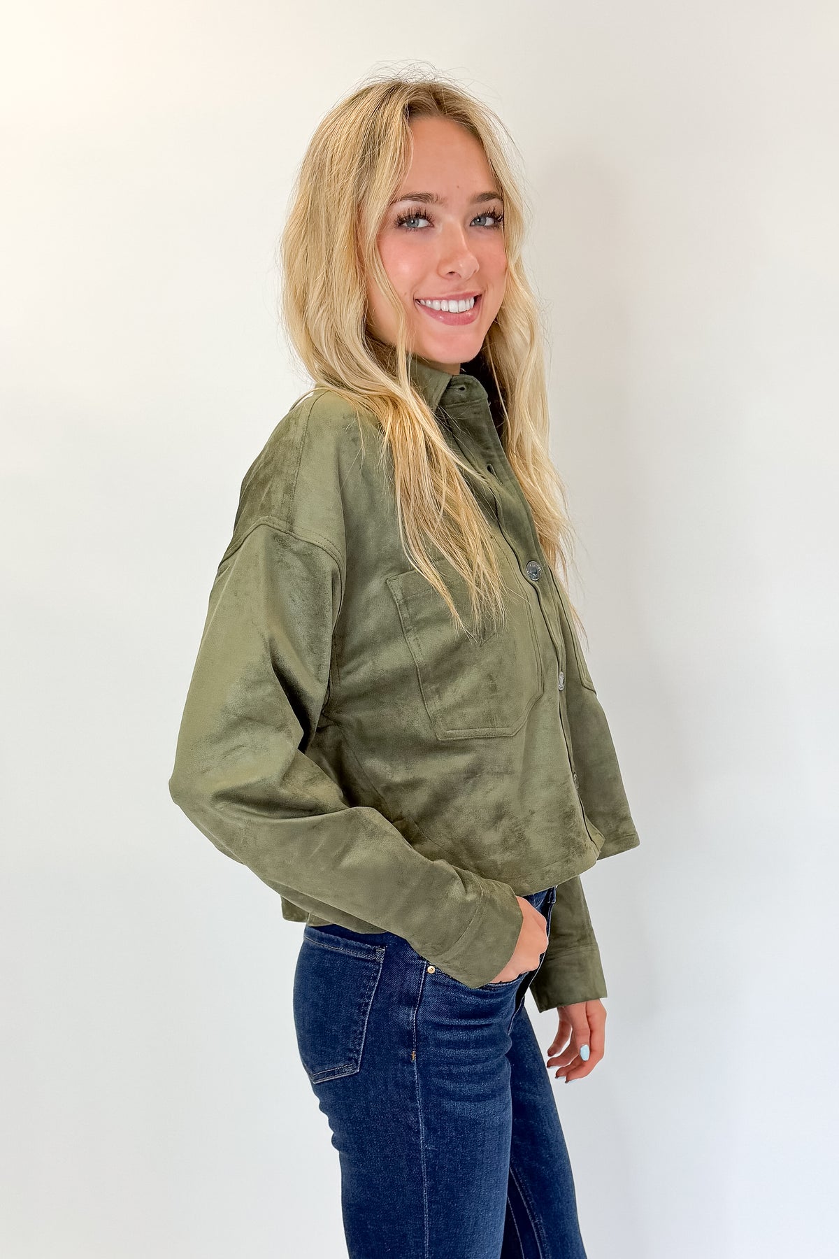 Side view of woman wearing Swagger Boutique’s Monstera All Day Cropped Suede Jacket by Z Supply with jeans against white studio background.