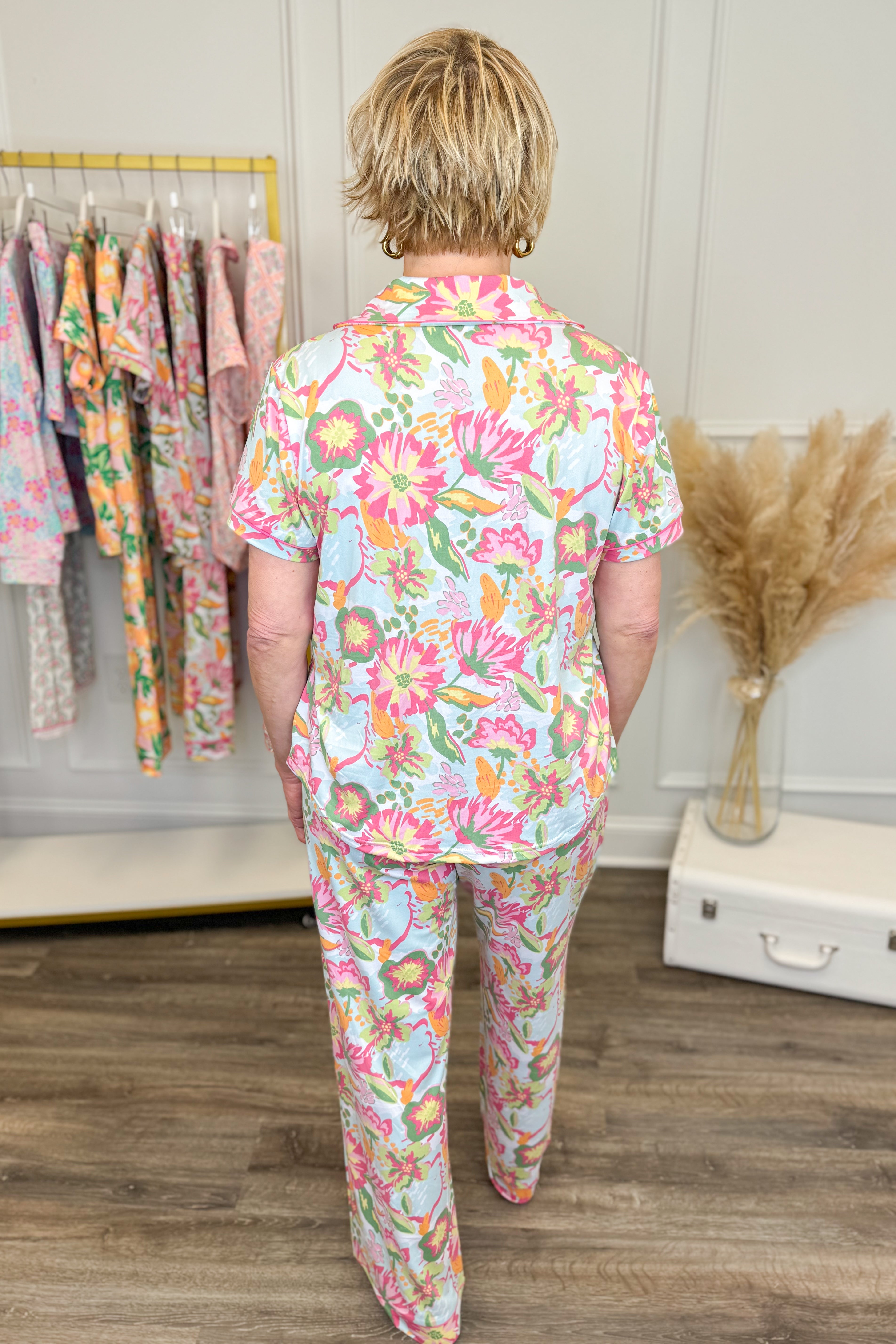 Person wearing a colorful floral pajama set standing in a room with a rack of clothes and decorative elements.