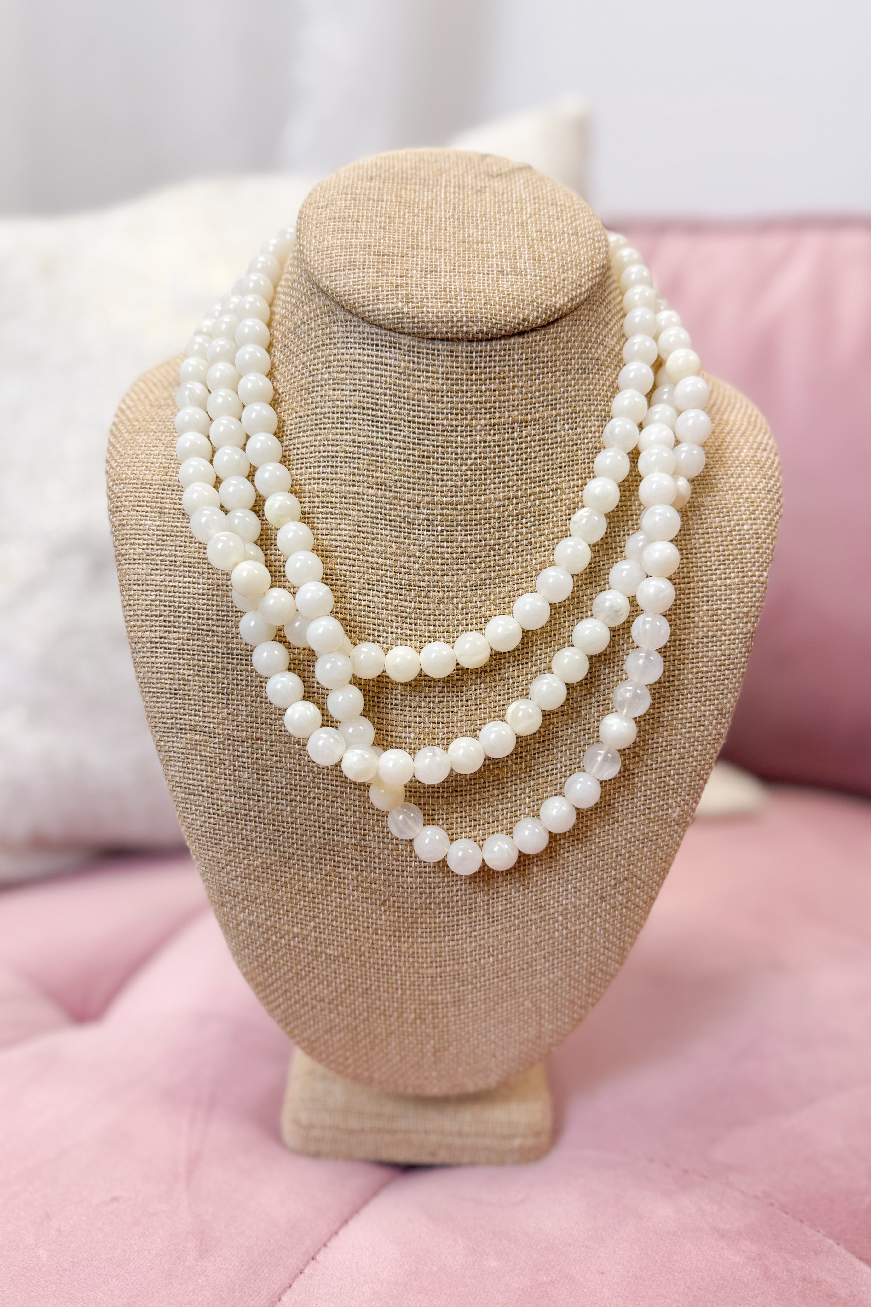 Necklace on a beige jewelry stand with a pink cushion background