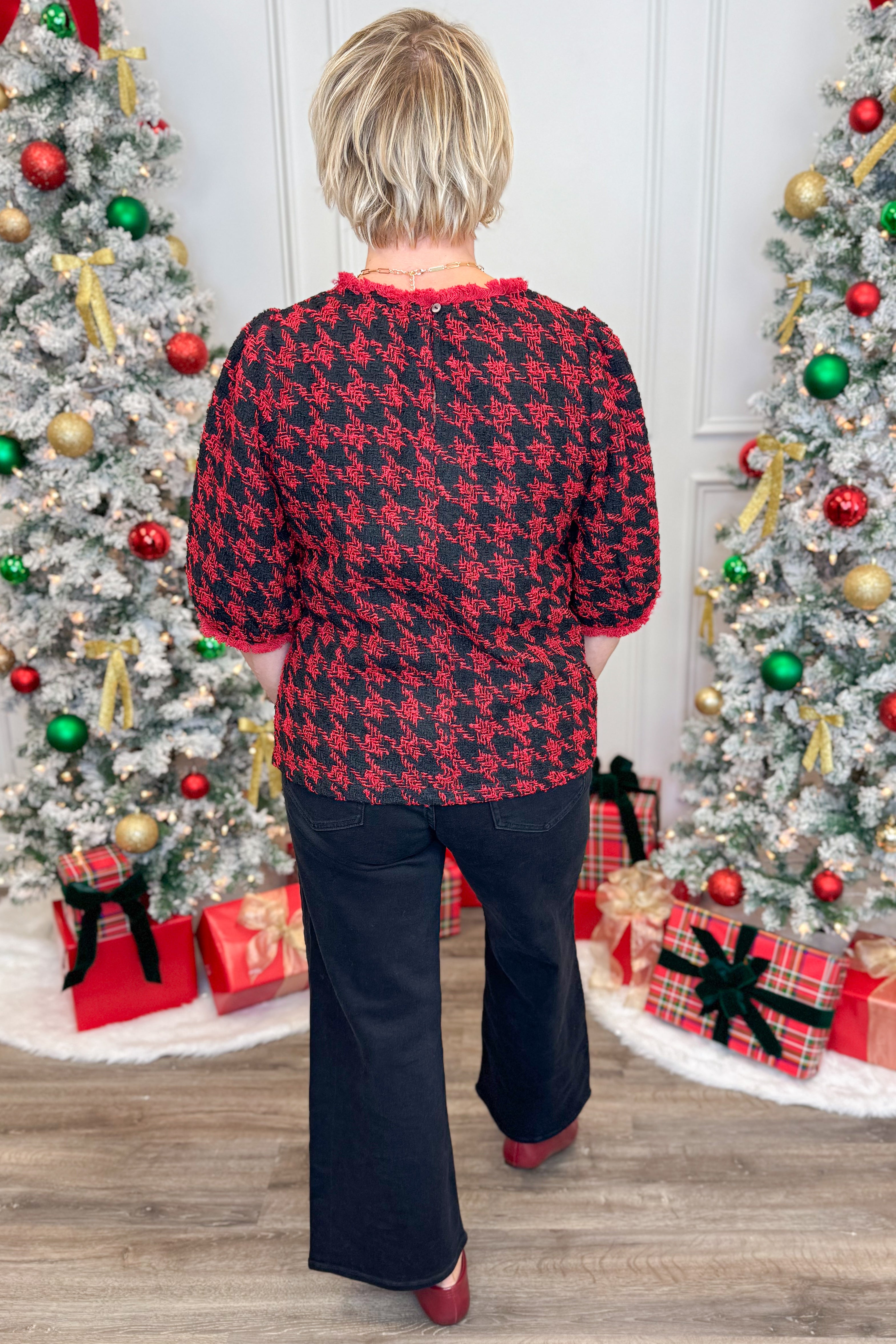 Person wearing a red and black patterned shirt in front of Christmas trees and presents.