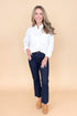 Front view of woman wearing white collared shirt with jeans against a tan background.