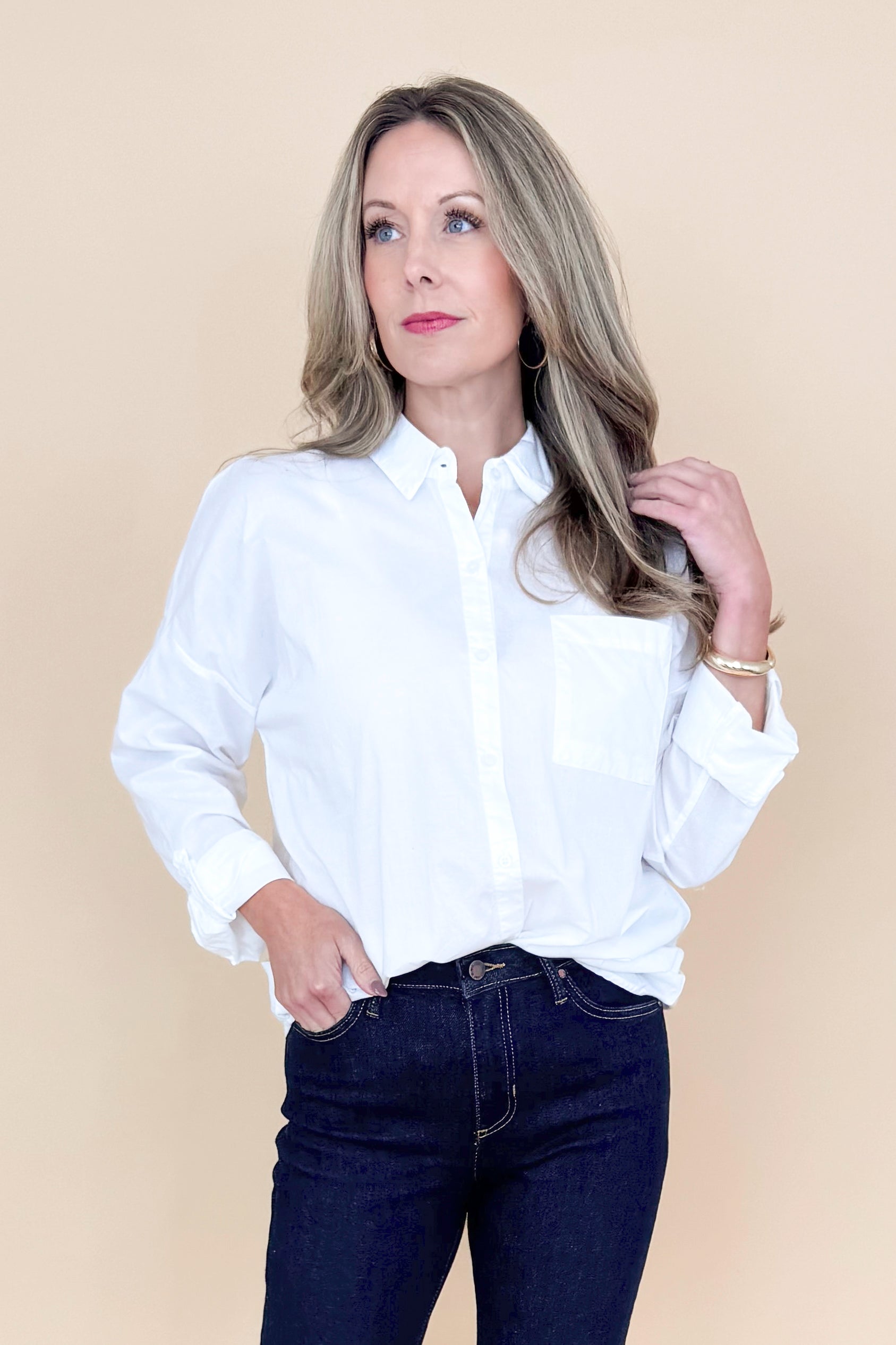 Front view of woman wearing white collared shirt with jeans against a tan background.
