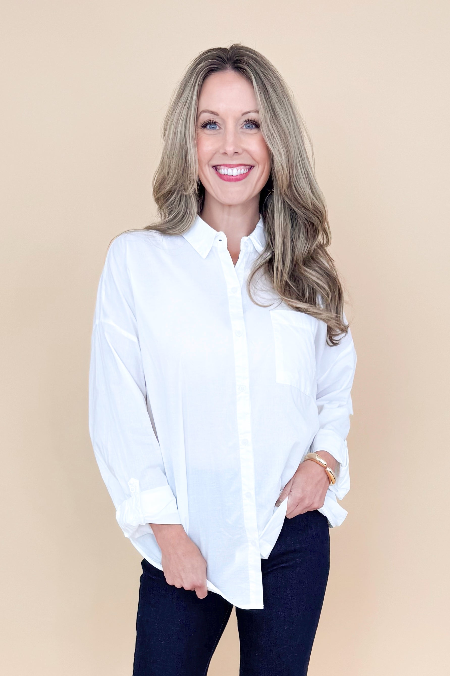 Front view of woman wearing white collared shirt with jeans against a tan background.