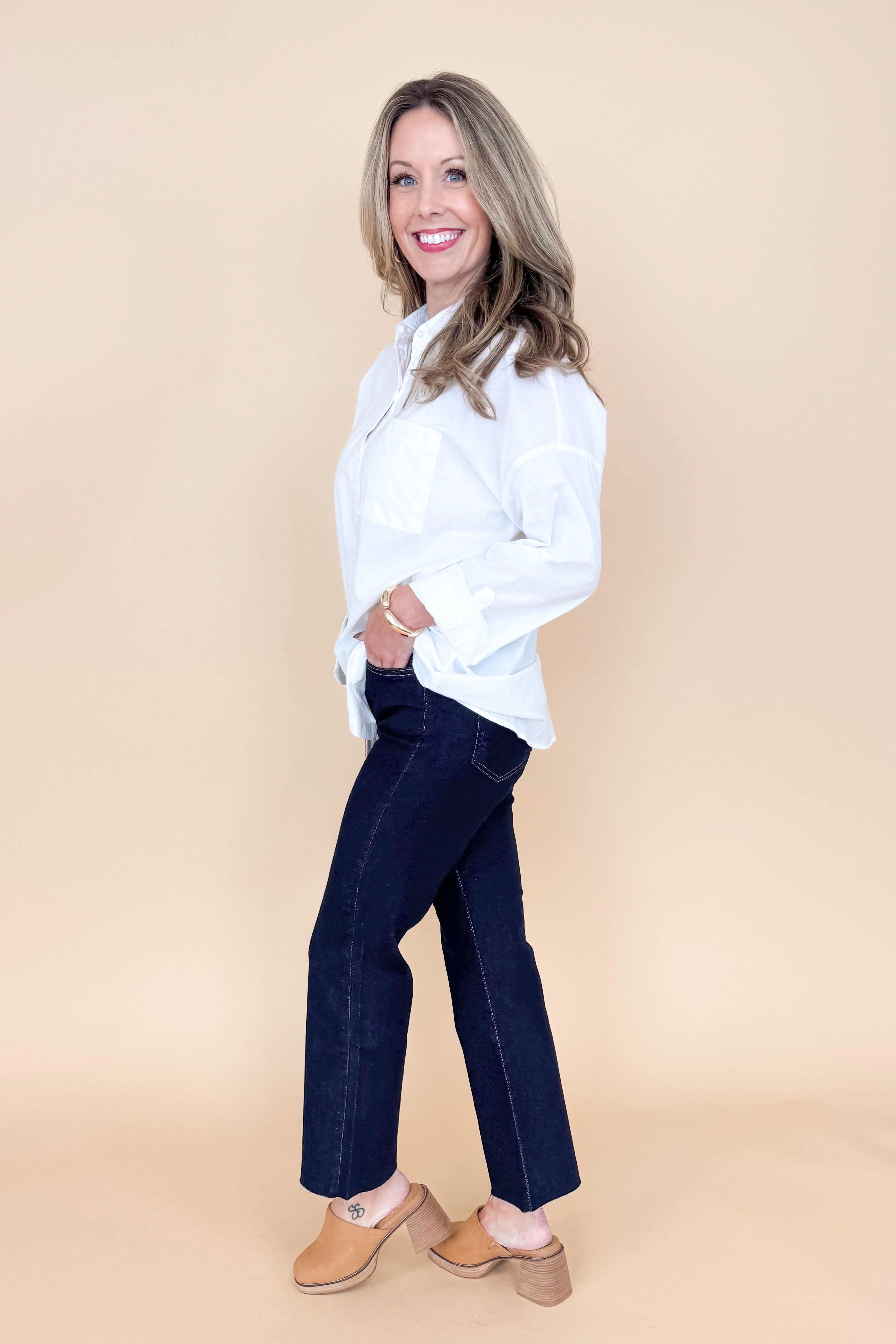 Side view of woman wearing white collared shirt with jeans against a tan background.