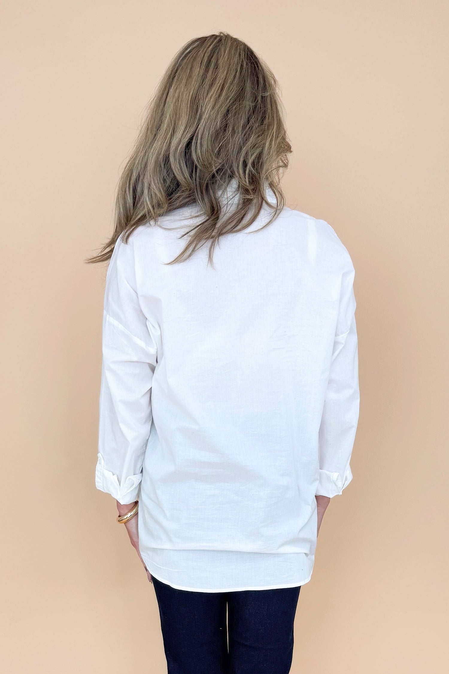 Back view of woman wearing white collared shirt with jeans against a tan background.