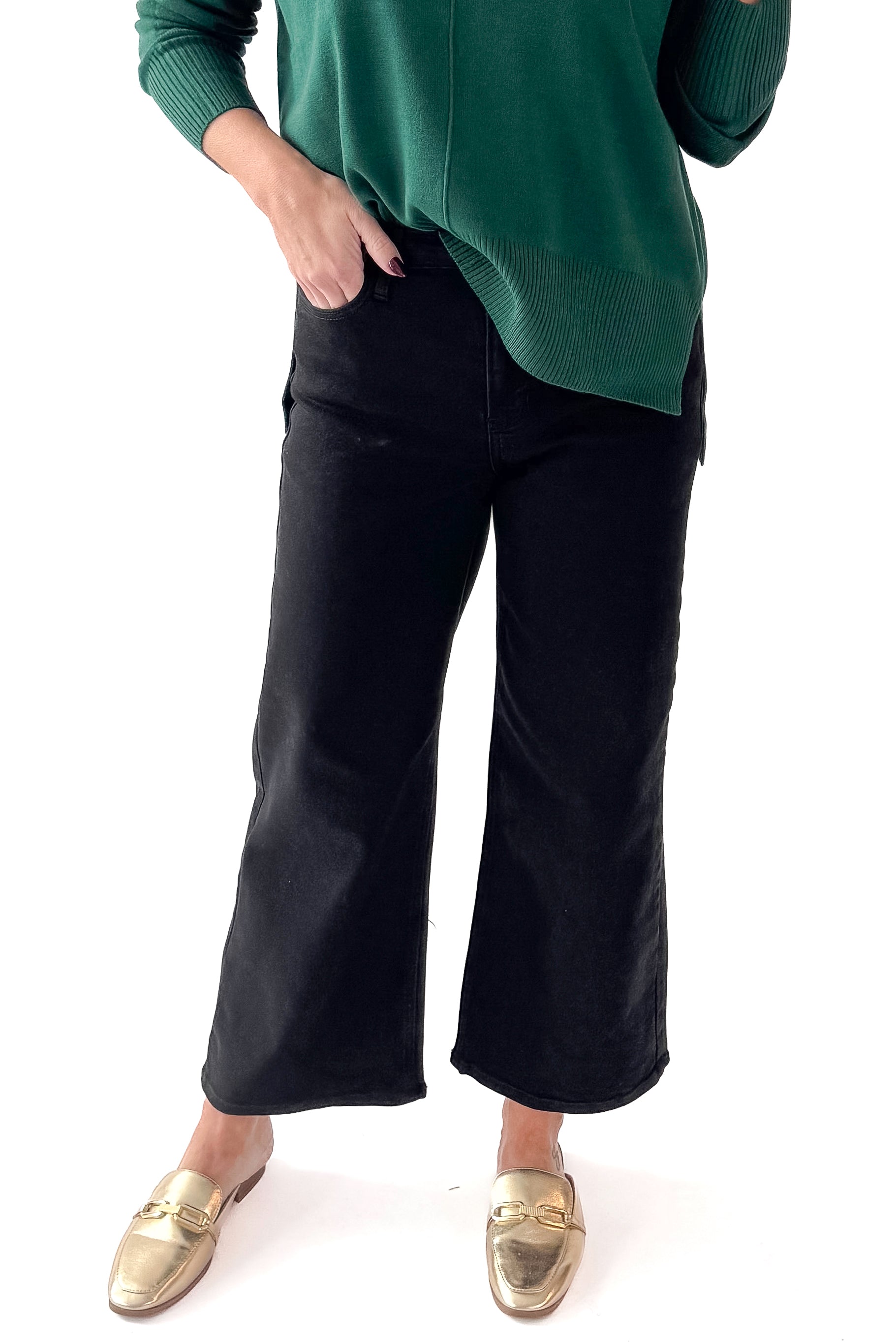 Front view of woman wearing green top with black wide leg jeans against white studio background.