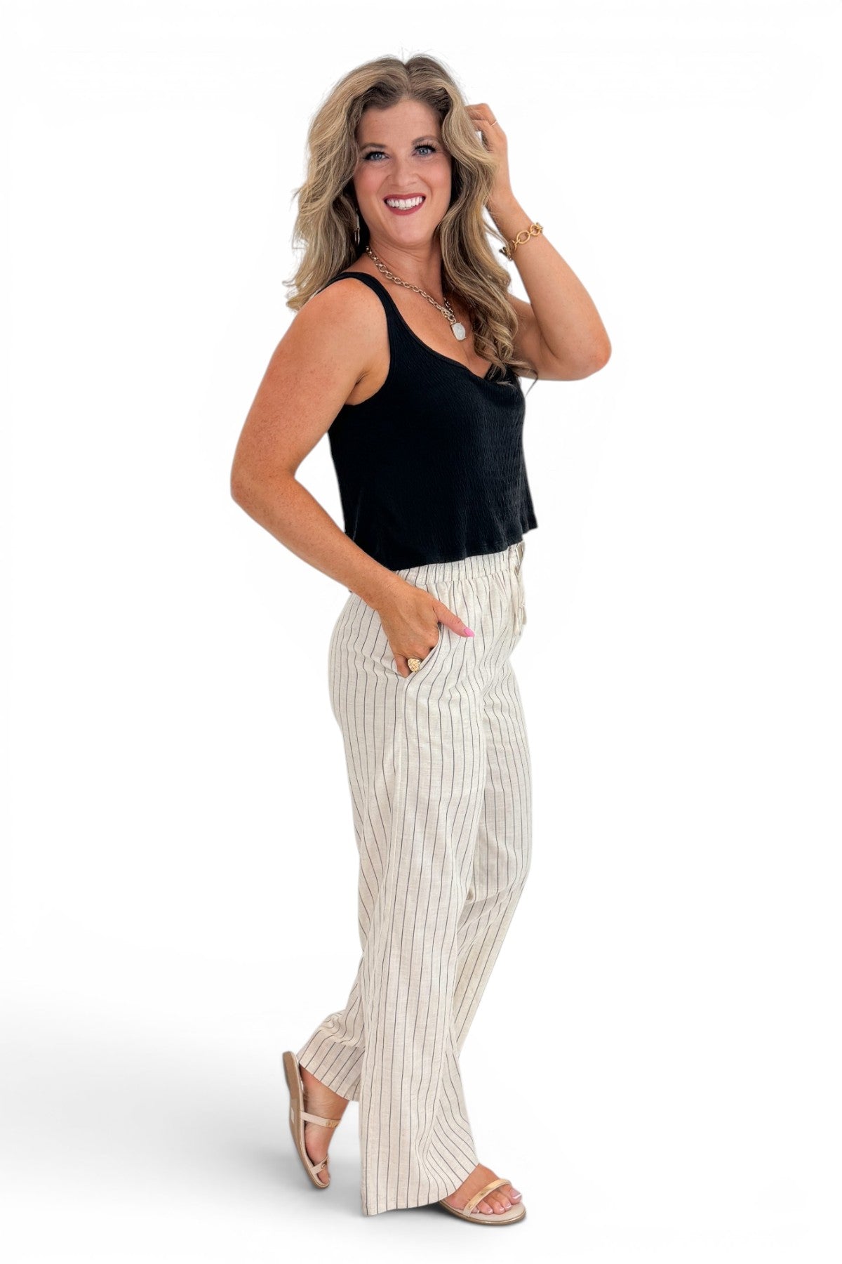 Side view of woman wearing Swagger Boutiqueβs Beige Striped Wide Leg Linen Pants with top against white studio background.