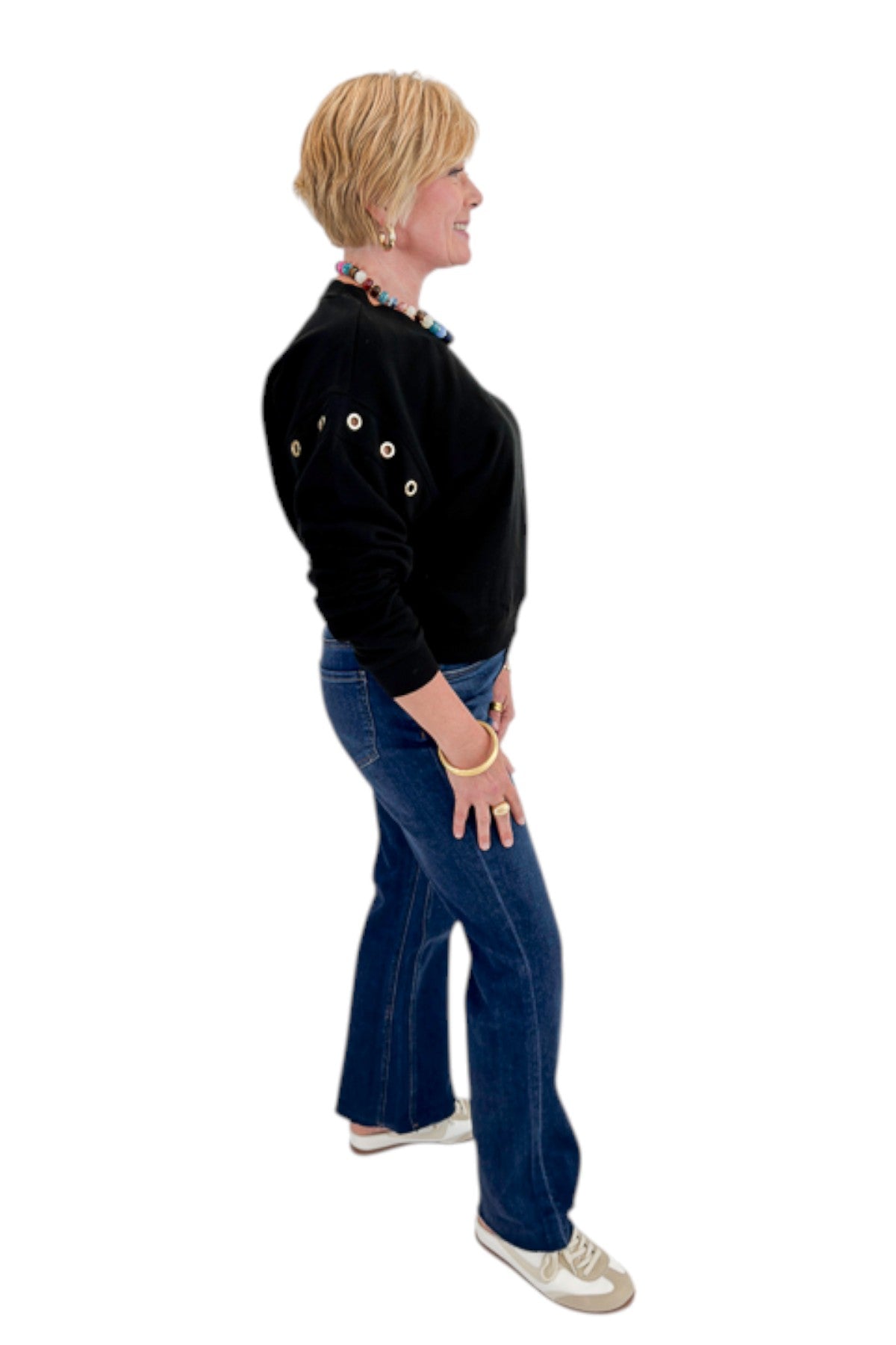 Side view of woman wearing Swagger Boutiqueās Black Axel Grommet Sweatshirt by Z Supply with jeans against white studio background.