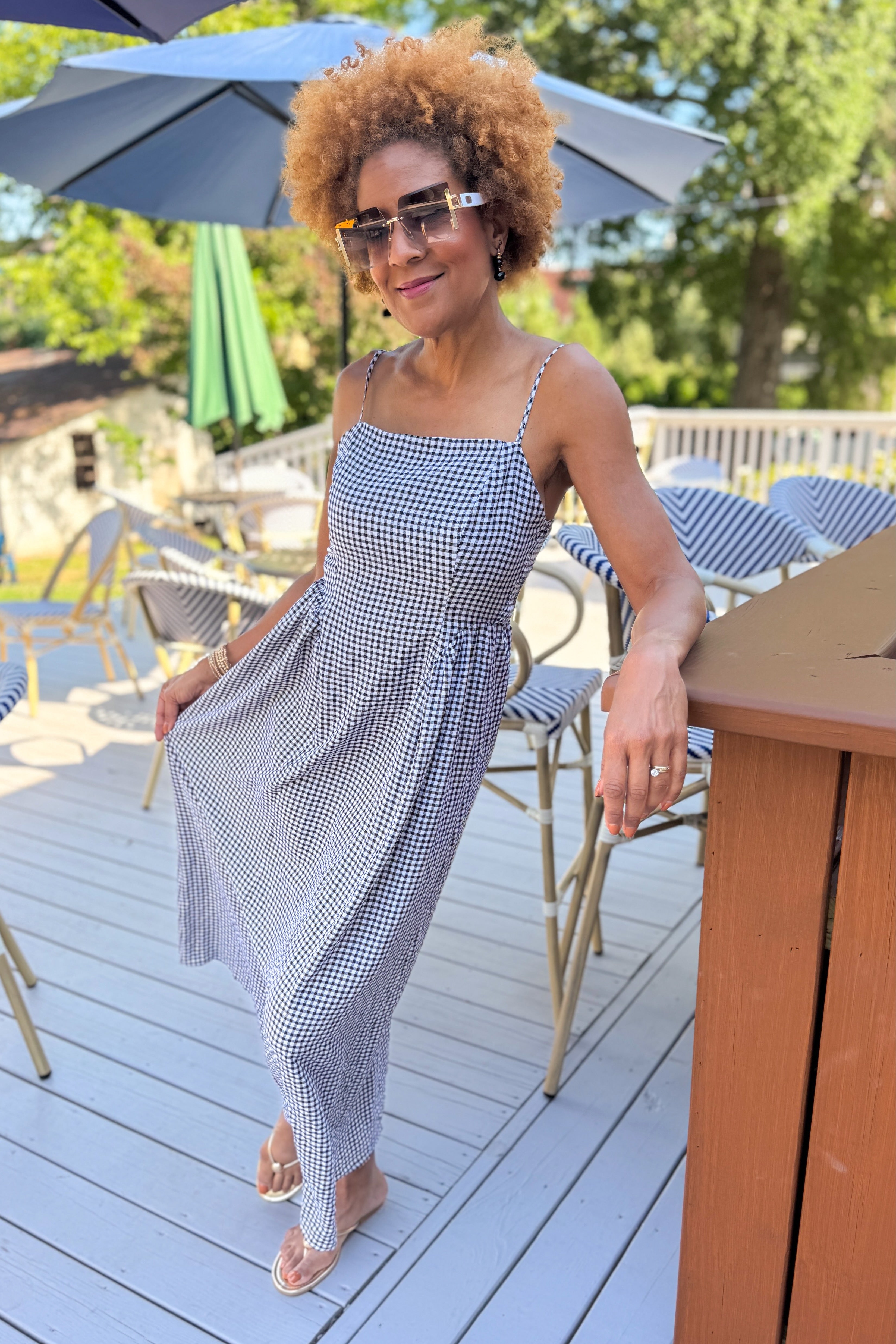 Front view of woman wearing Swagger Boutique’s Black Gingham Maxi Dress with sandals standing outside at a restaurant.