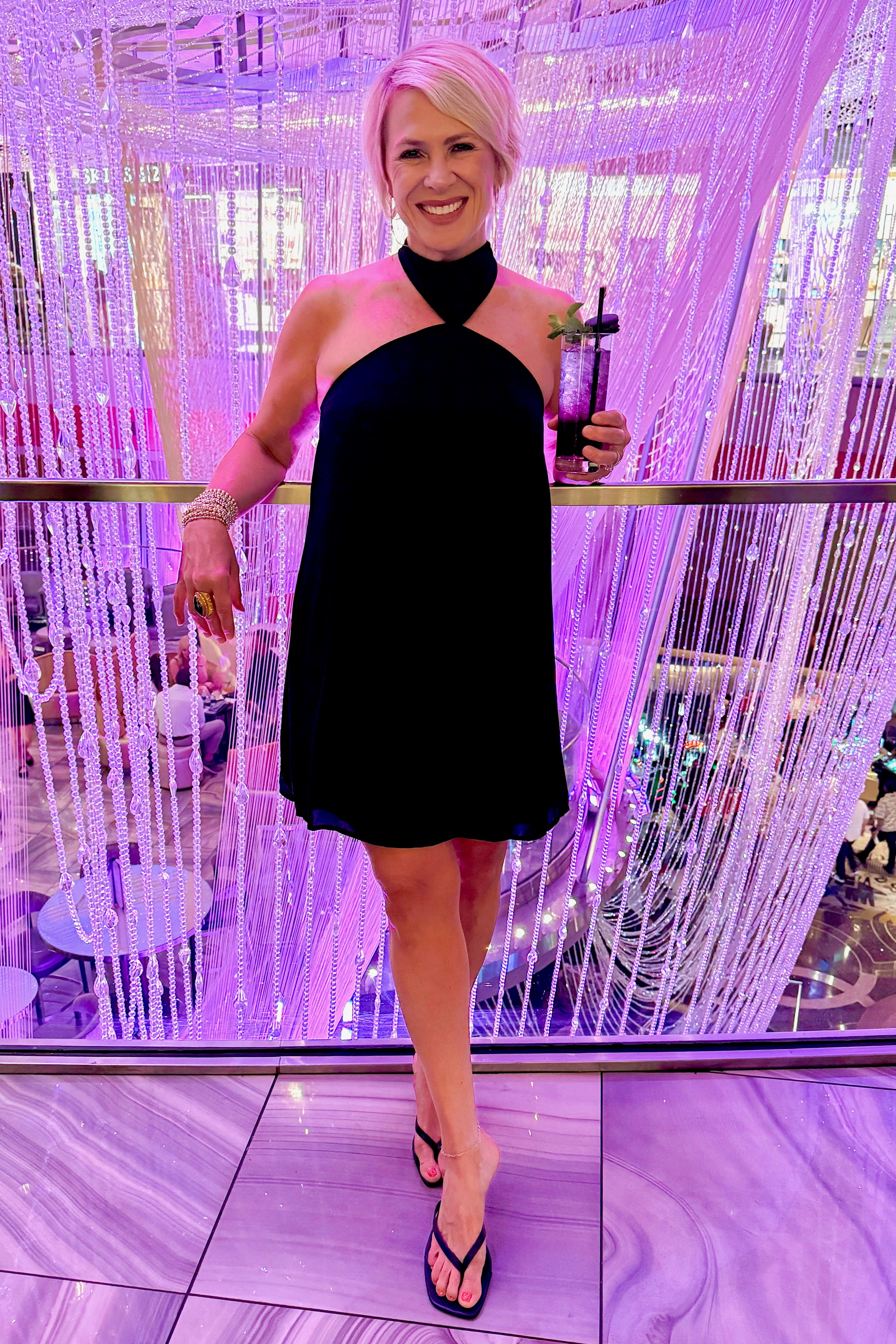 Front view of woman wearing Swagger Boutiqueās Black Halter Neck Mini Dress with heels at a fancy restaurant.