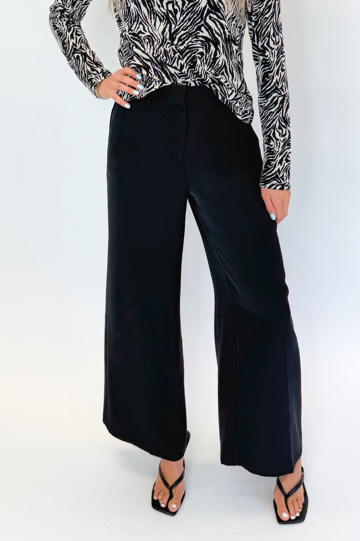 Front detail view of woman wearing Swagger Boutique’s Black High Waisted Trousers by Skies Are Blue & Zebra Mock Neck Long Sleeve Top by Entro against white studio background.