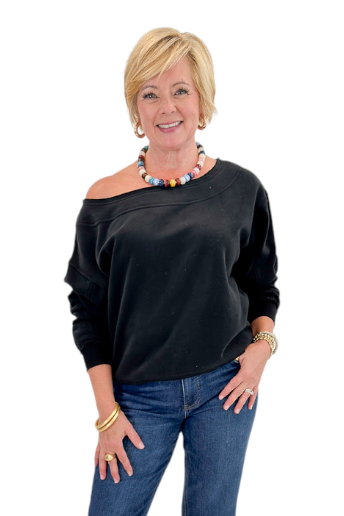 Front view of woman wearing Swagger Boutiqueās Black Off The Shoulder Sweatshirt with jeans against white studio background.