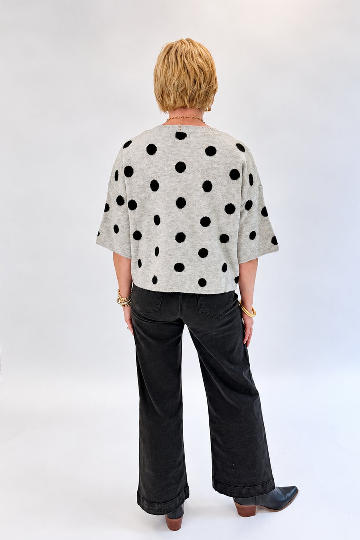 Back view of woman wearing Swagger Boutique’s Black Pintuck Jeans by Risen with sweater against white studio background.