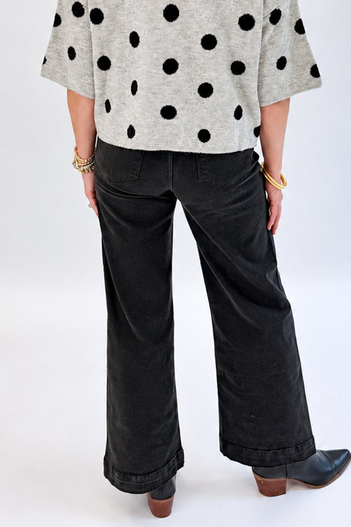 Back view of woman wearing Swagger Boutique’s Black Pintuck Jeans by Risen with sweater against white studio background.