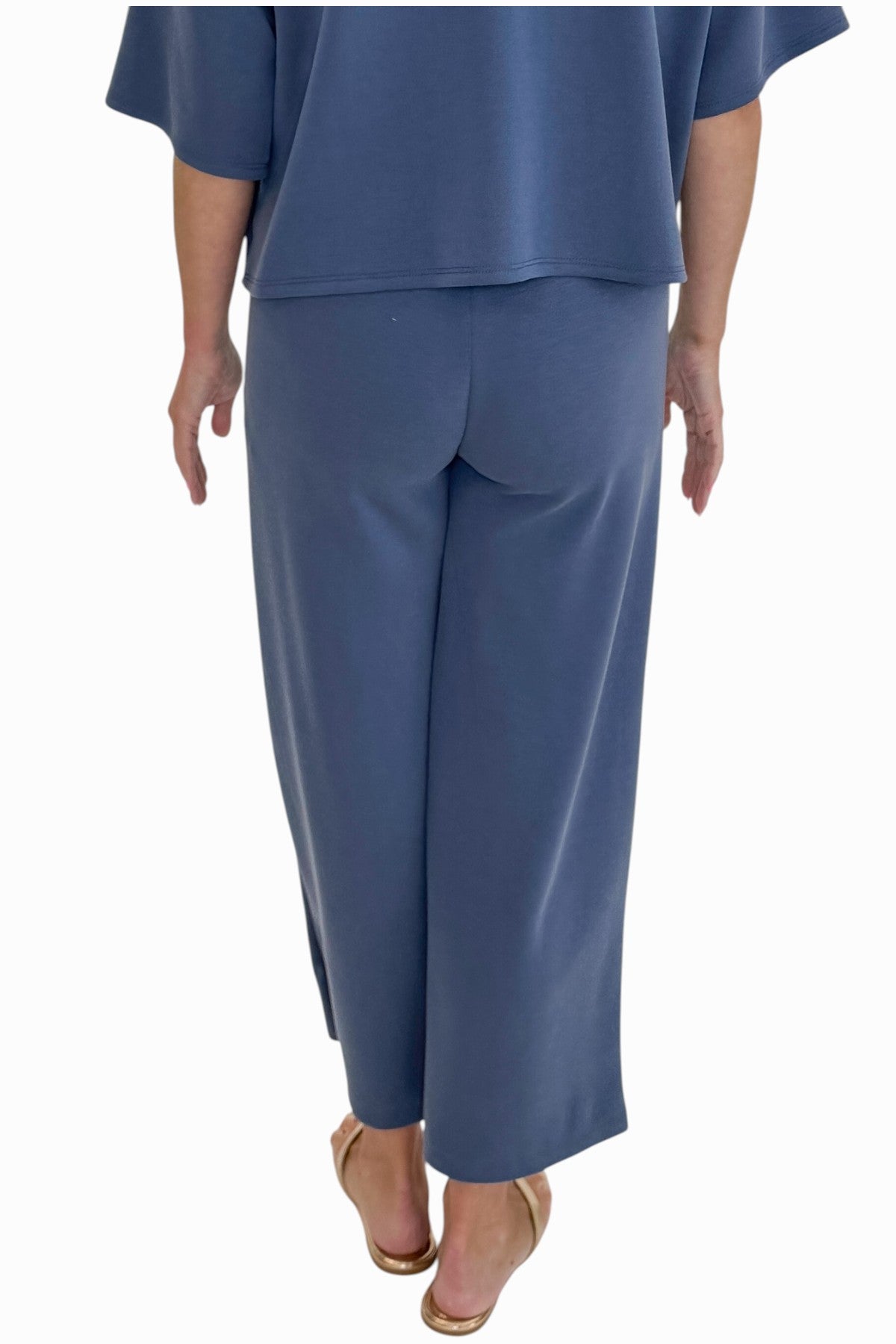 Back detail view of woman wearing Swagger Boutiqueās Blue Cropped Lounge Pants and matching Blue Round Neck Short Sleeve Top against white studio background.
