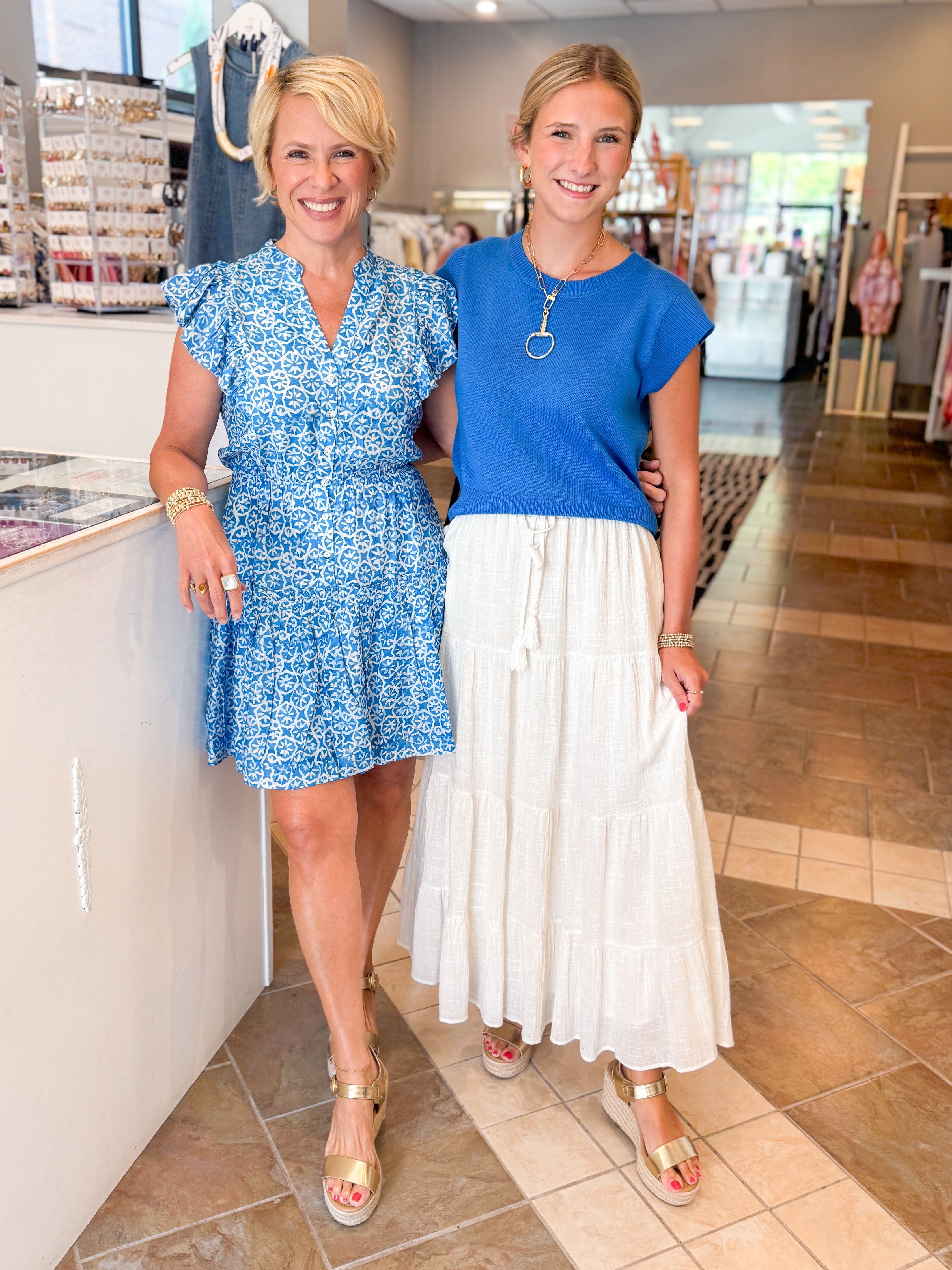 Front view of woman wearing Swagger Boutiqueās Blue Floral Print Mini Dress with sandals at the store with woman wearing skirt and sweater.