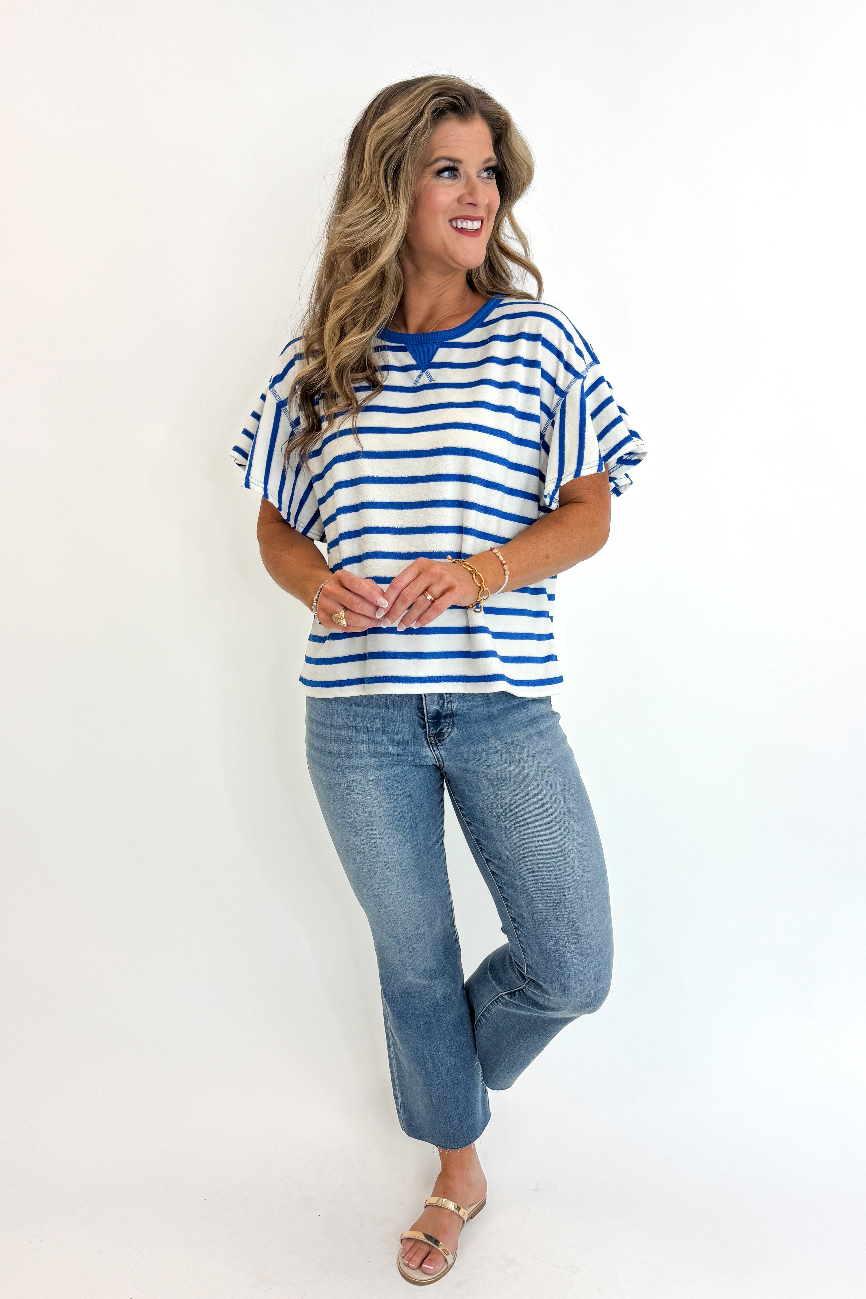 Front view of woman wearing Swagger Boutique’s Striped Flutter Sleeve Terry Top with jeans against white studio background.