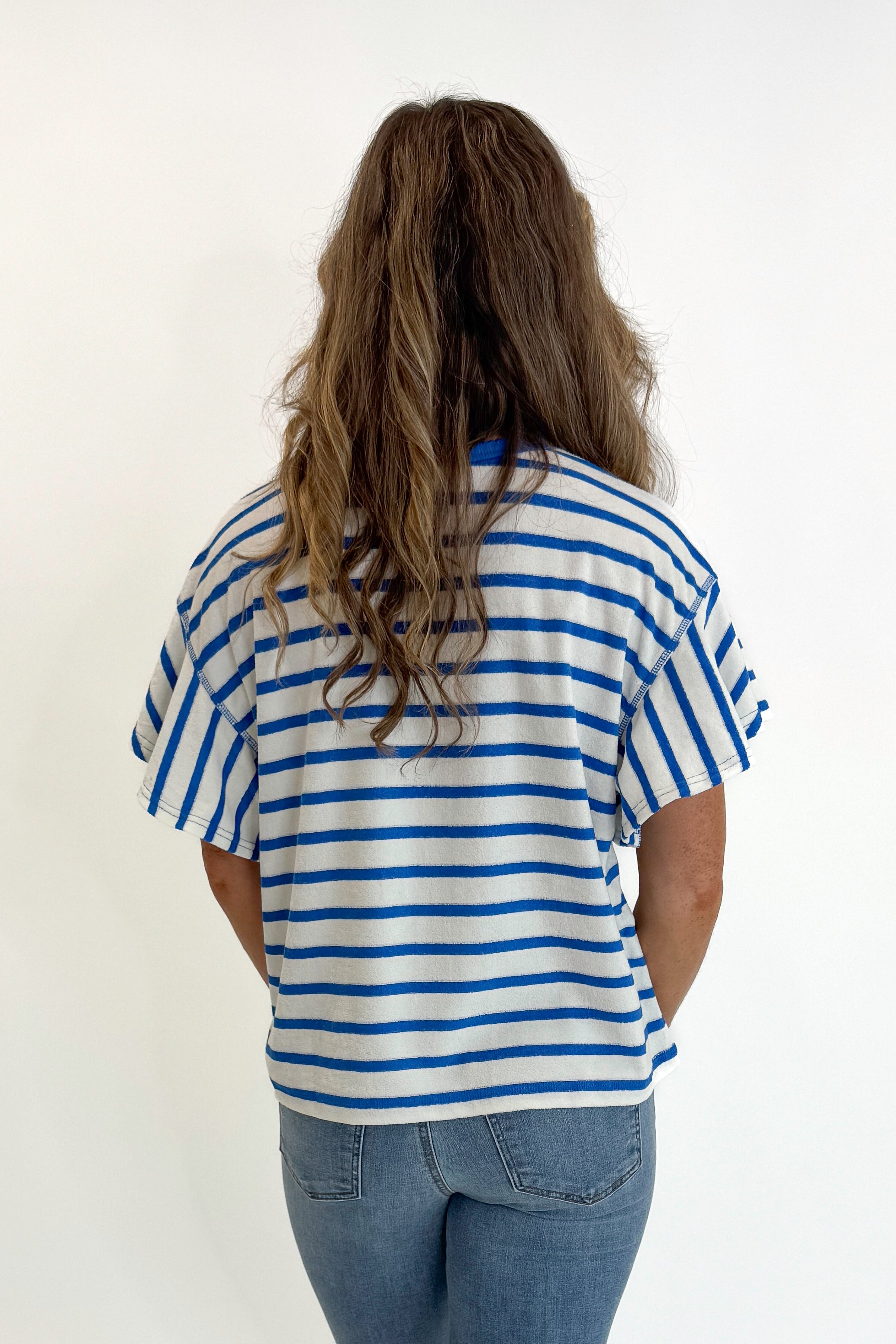 Back view of woman wearing Swagger Boutique’s Striped Flutter Sleeve Terry Top with jeans against white studio background.