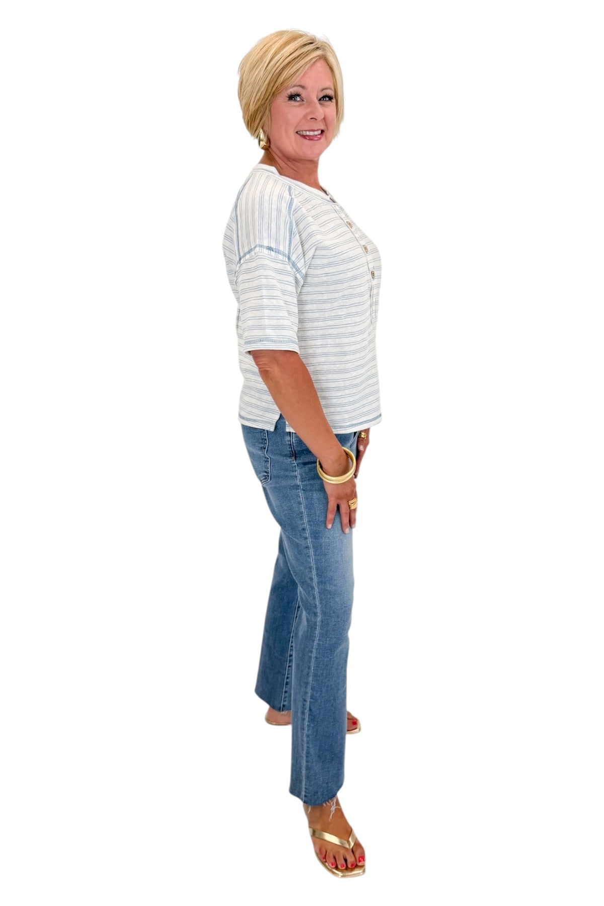 Side view of woman wearing Swagger Boutique’s Blue Striped Relaxed Fit Top with jeans against white studio background.