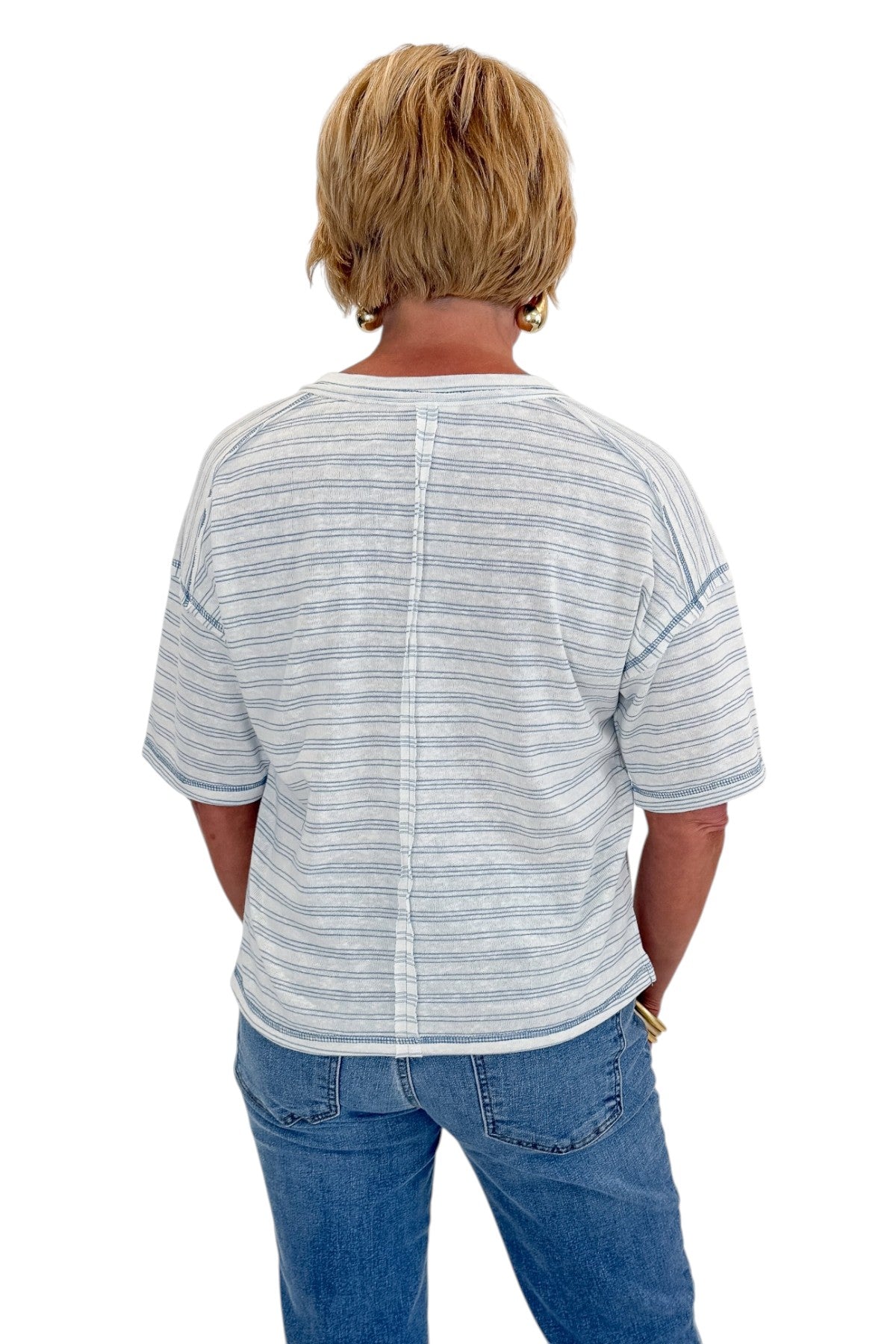 Back view of woman wearing Swagger Boutique’s Blue Striped Relaxed Fit Top with jeans against white studio background.