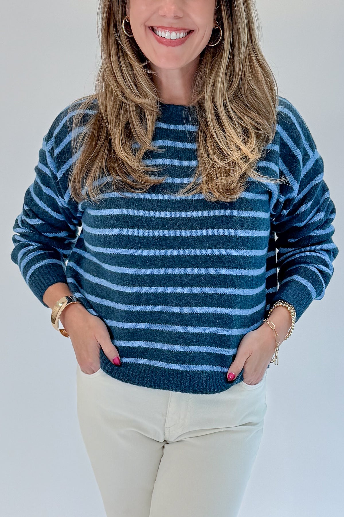 Front detail view of woman wearing Swagger Boutique’s Blue Striped Sweater with jeans against white studio background.