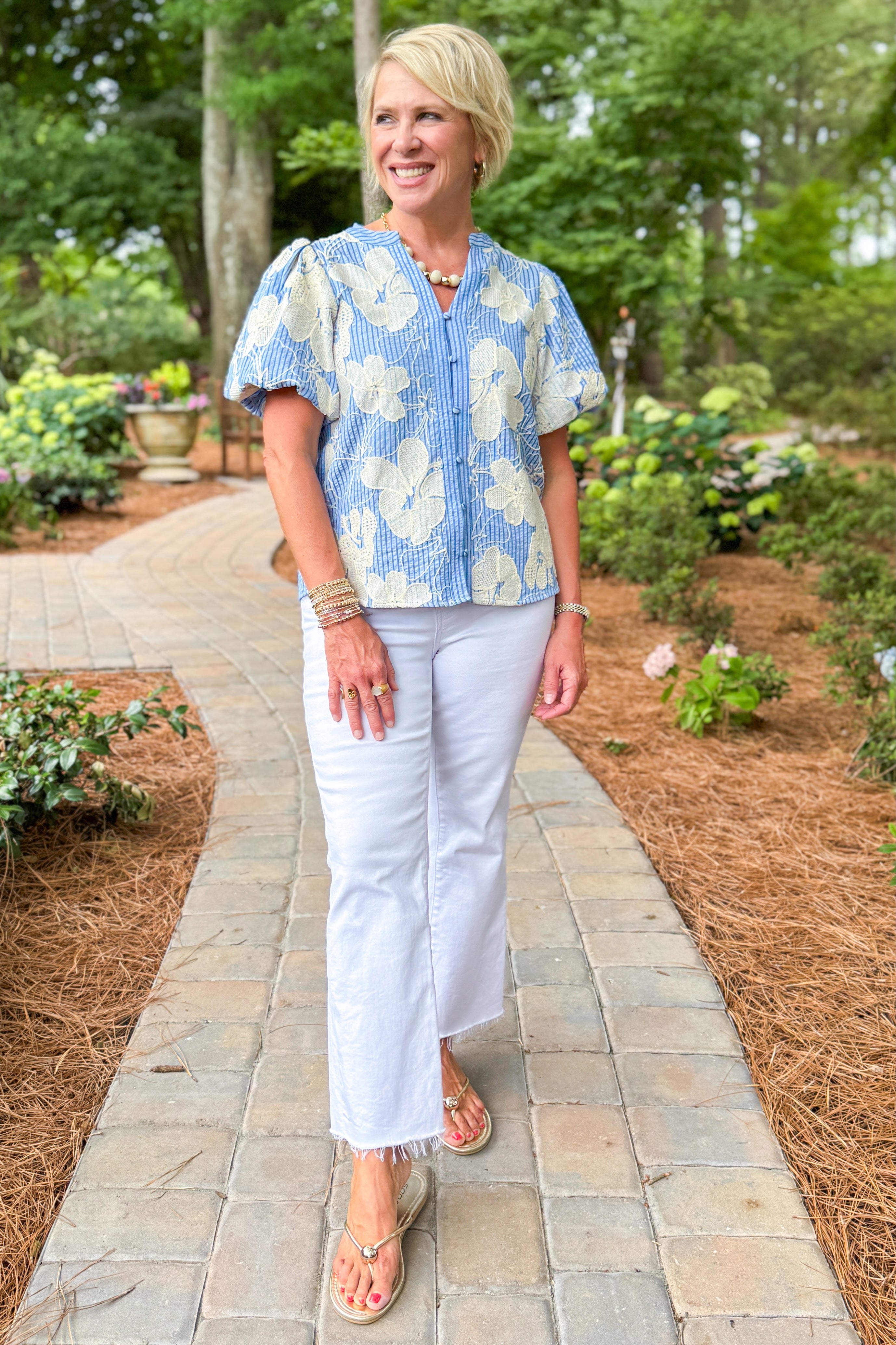 Woman wearing a blue floral blouse and white jeans walking down a path.