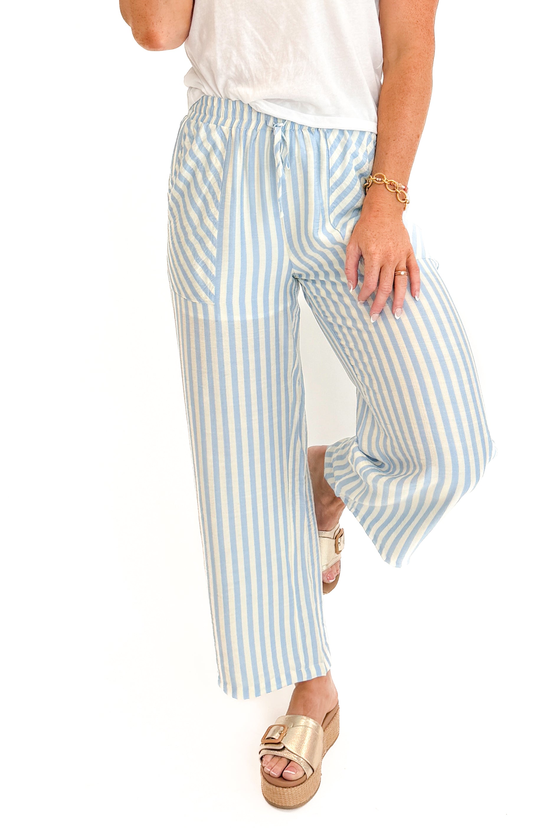 Front detail view of woman wearing Swagger Boutique’s Blue & Cream Striped Pants with white top against white studio background.