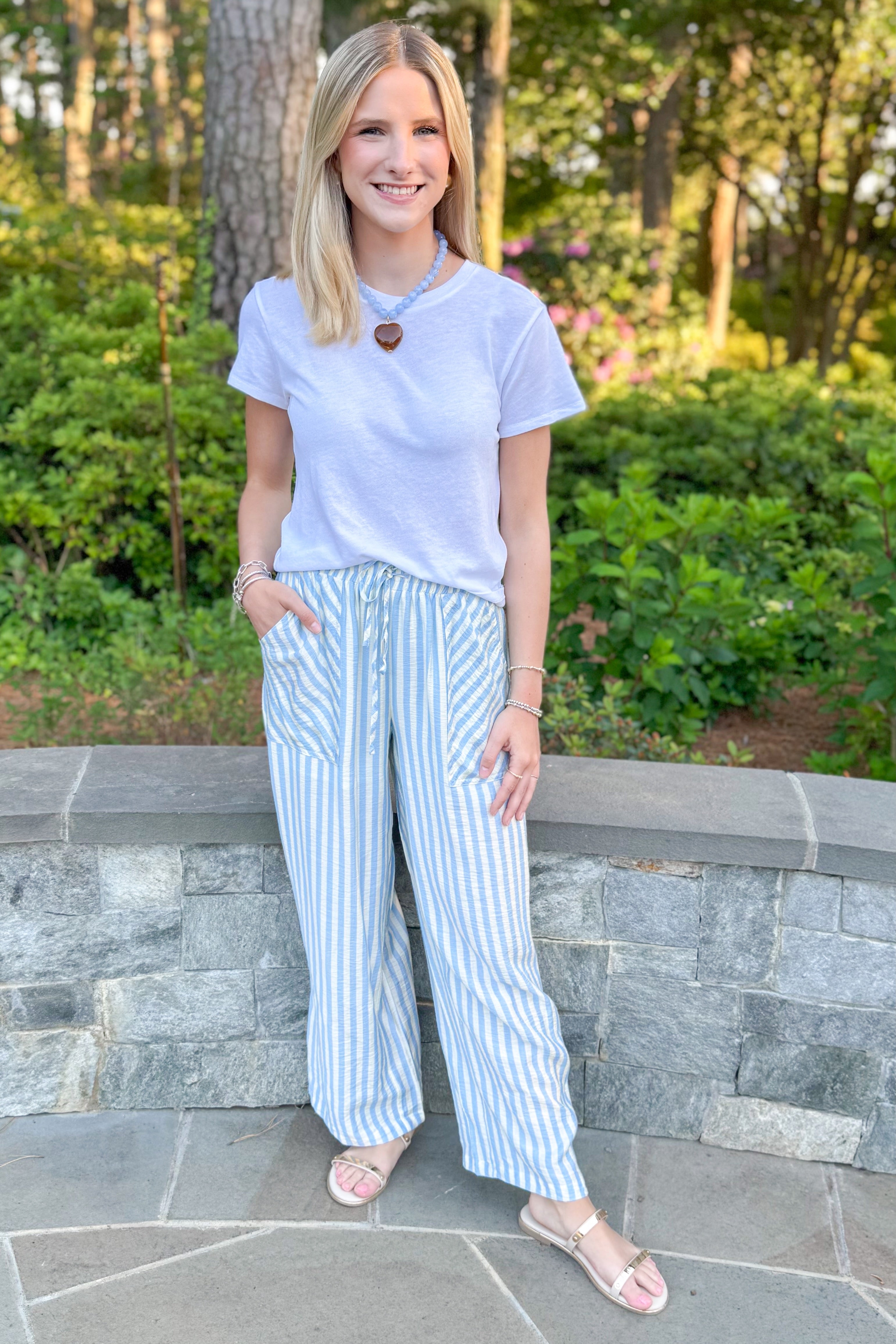 Front view of woman wearing Swagger Boutique’s Blue & Cream Striped Pants with white top standing outside.