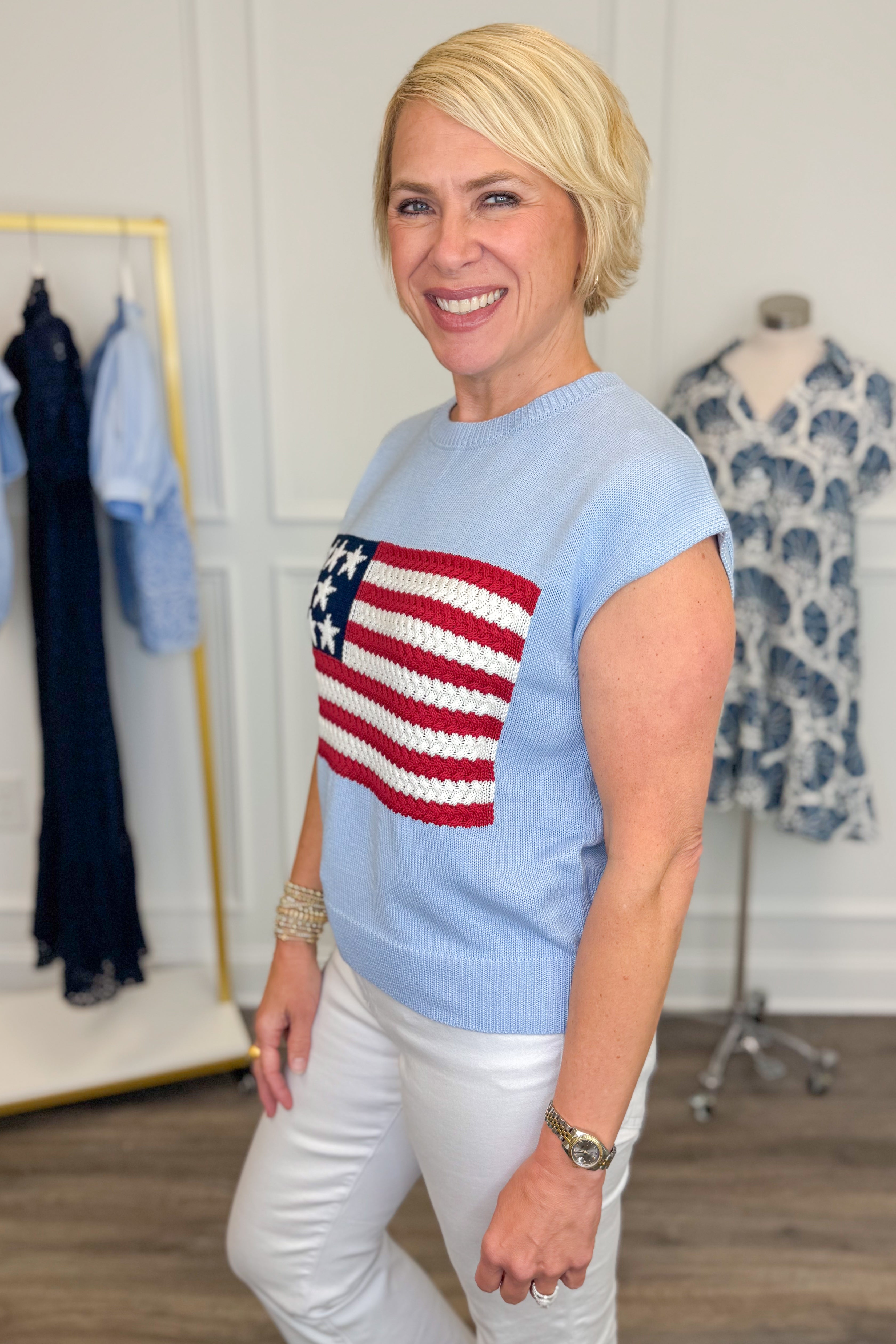 Side view of woman wearing Swagger Boutique’s Blue Flag Cap Sleeve Sweater with jeans against white studio background.