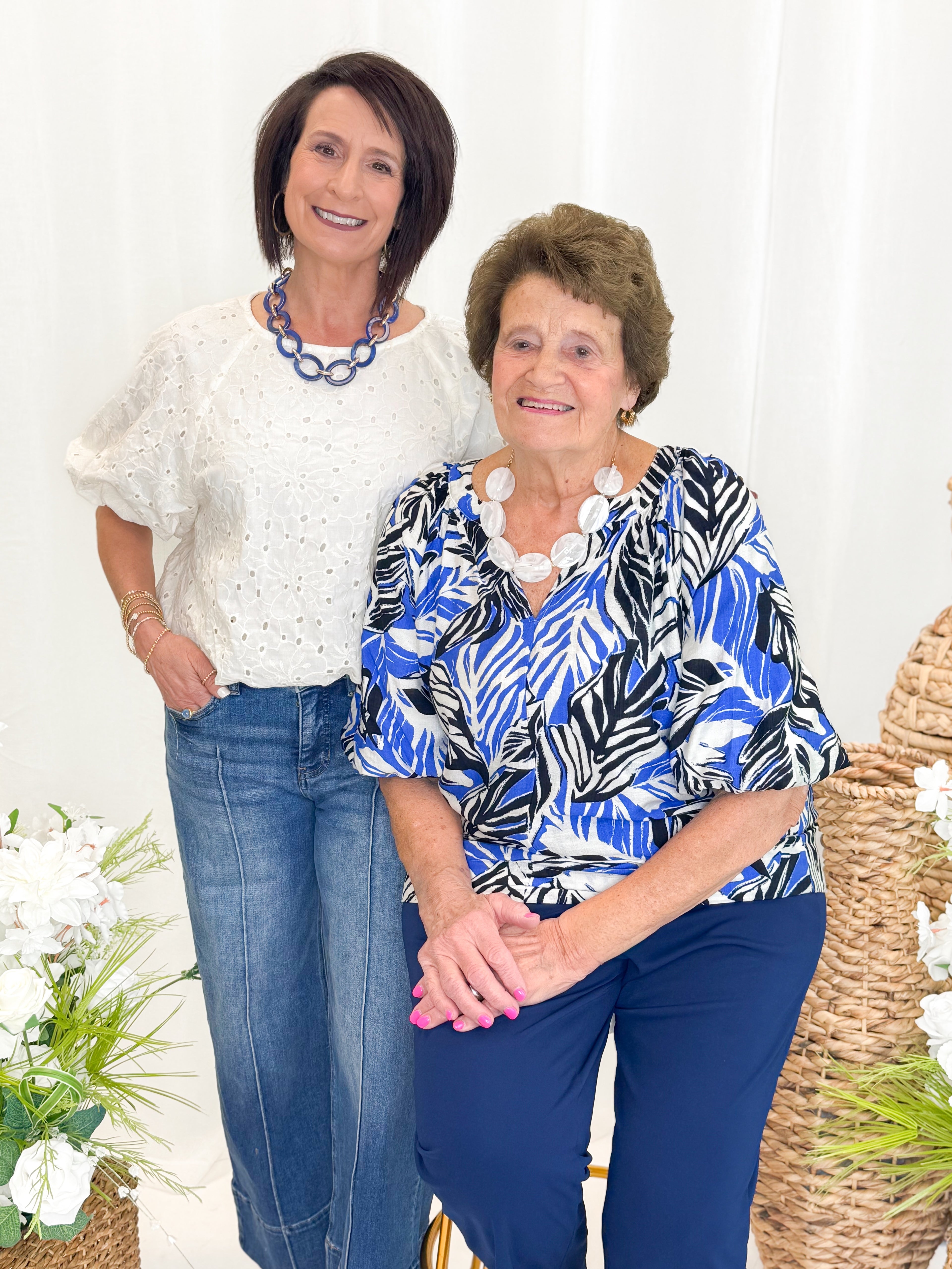 Front view of woman wearing Swagger Boutiqueās Blue & Navy Tropical Printed 3/4 Sleeve Top with blue pants against decorative background.