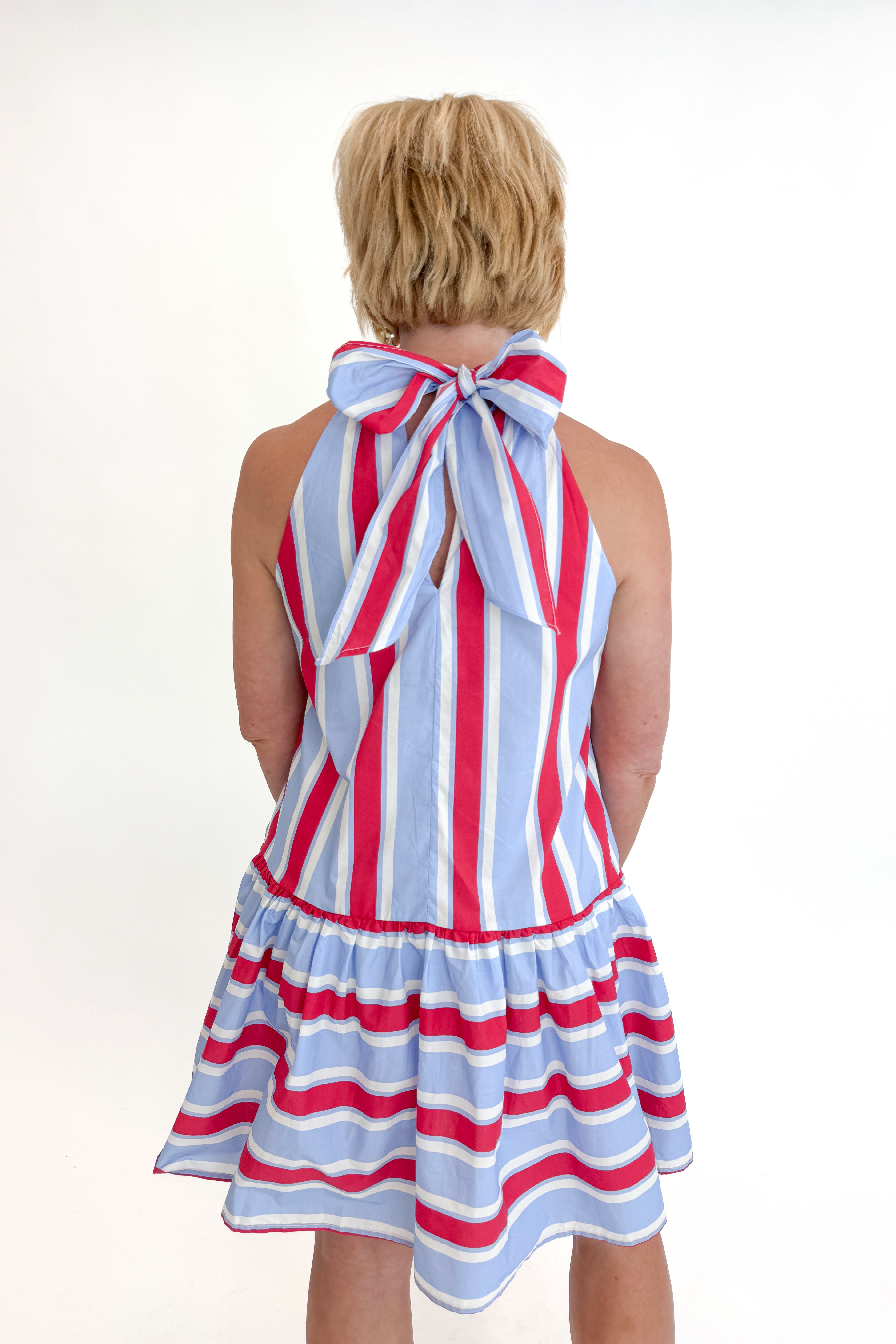 Back view of woman wearing Swagger Boutique’s Blue & Red Striped Halter Neck Dress by Entro with sandals against white studio background.