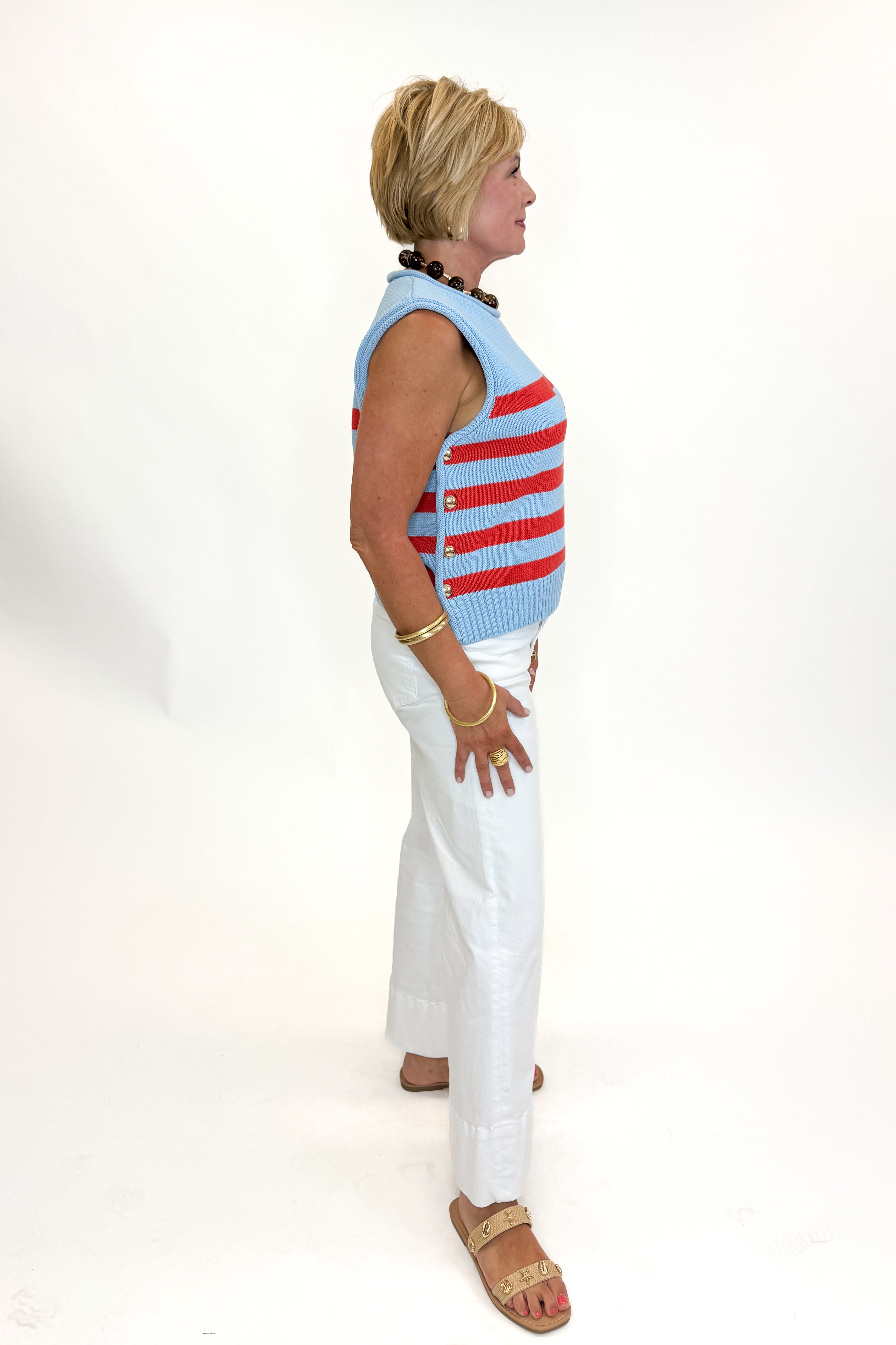Side view of woman wearing Swagger Boutique’s Blue & Red Striped Sleeveless Sweater by Entro with jeans against white studio background.