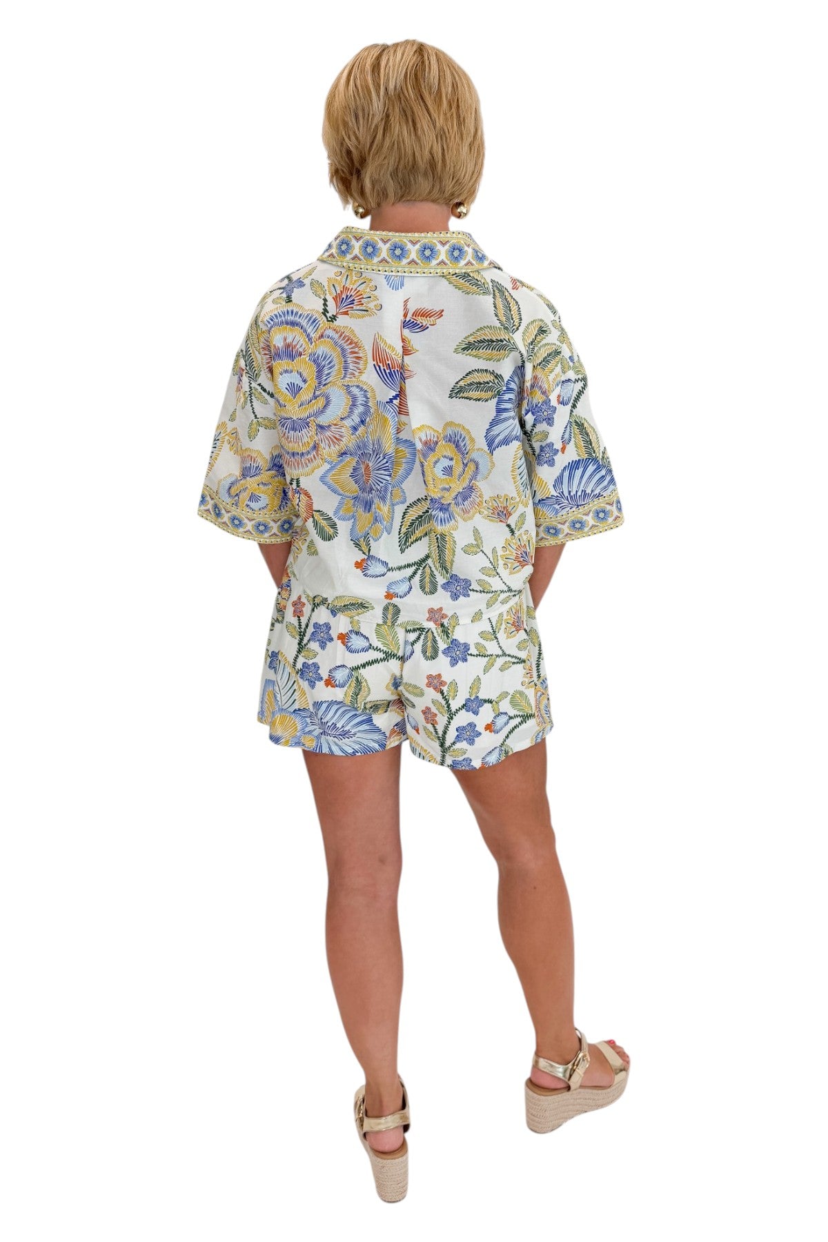 Back view of woman wearing Swagger Boutiqueās Blue & Yellow Floral Print Wrap Skort by Entro with matching top against white studio background.