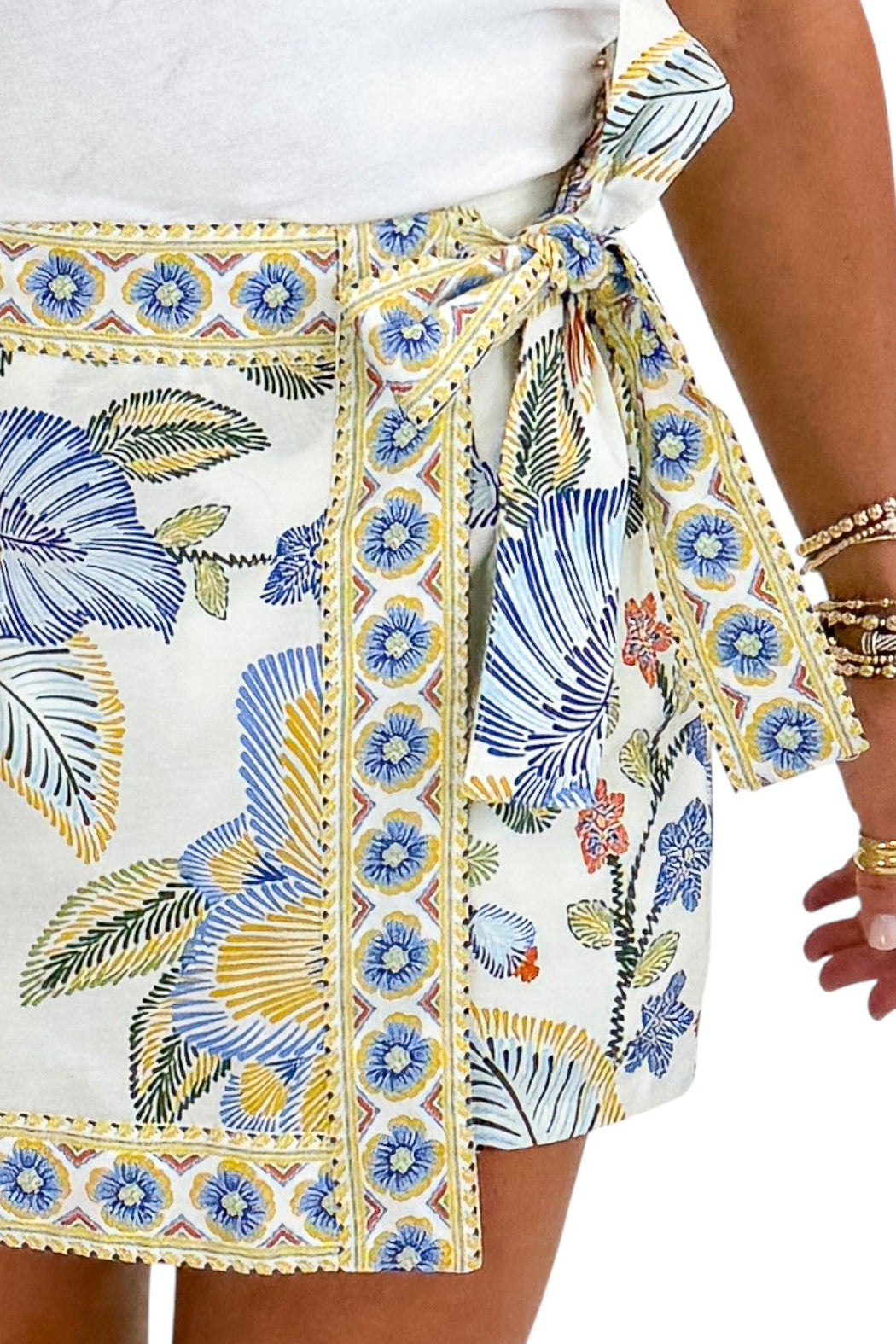 Front detail of woman wearing Swagger Boutiqueās Blue & Yellow Floral Print Wrap Skort by Entro with white top against white studio background.