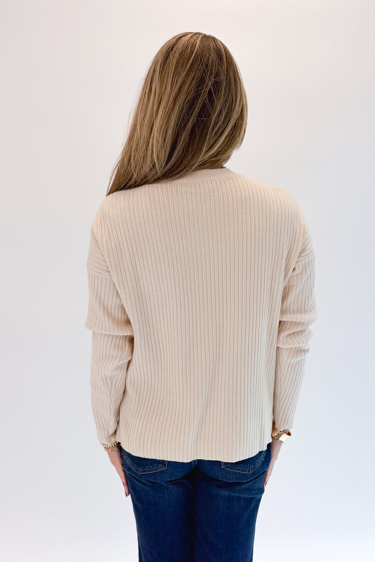 Back view of woman wearing Swagger Boutique’s Bone Ribbed Lightweight Sweater with jeans against white studio background.