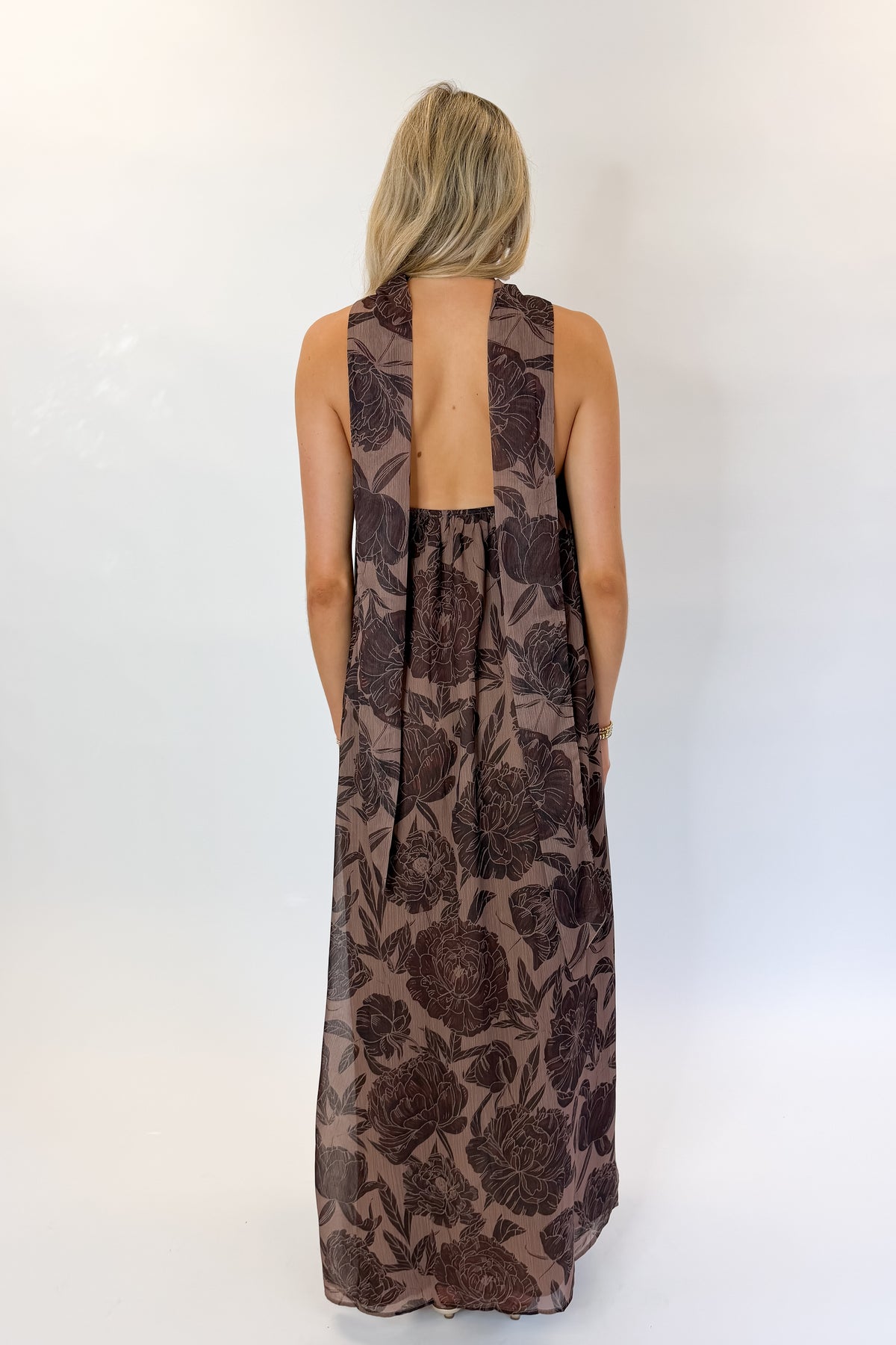 Back view of woman wearing Swagger Boutique’s Brown Floral Strapless Maxi Dress with heels against white studio background.