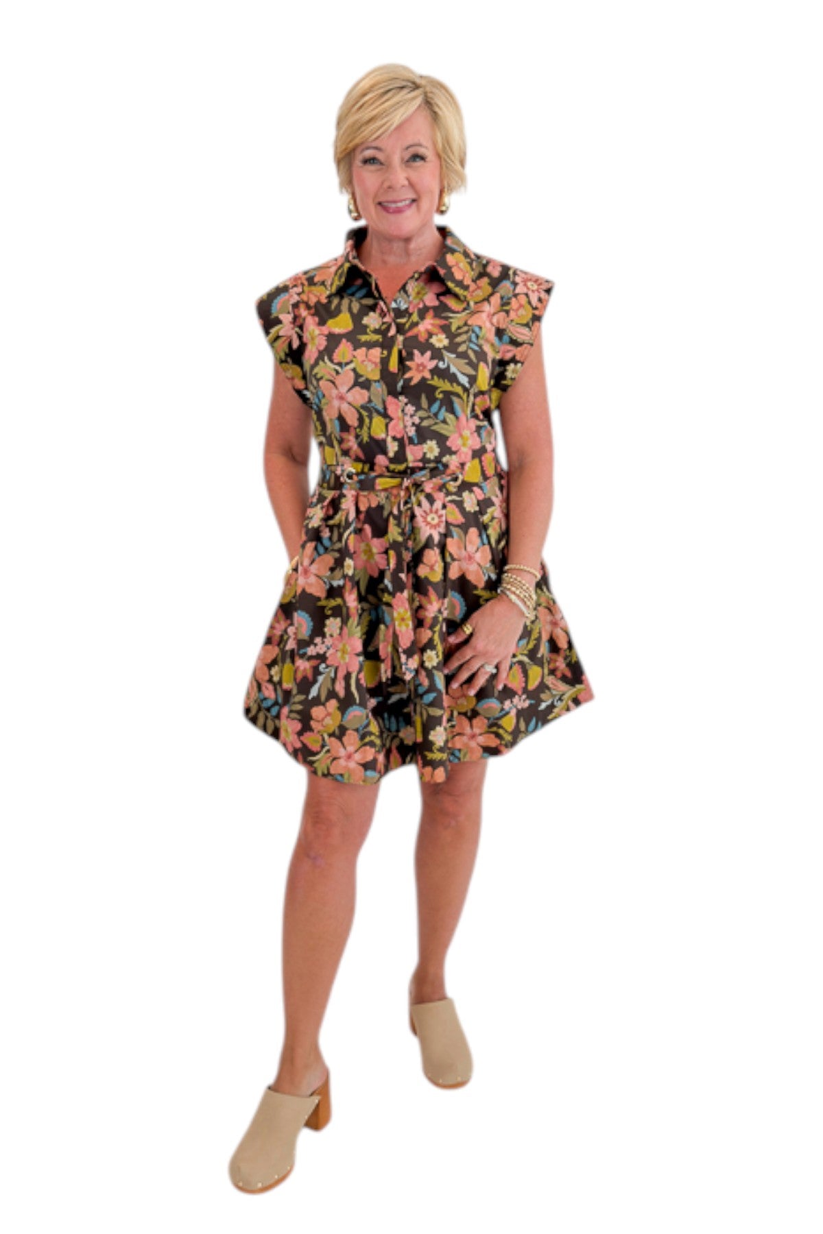 Front view of woman wearing Swagger Boutiqueās Brown Floral Tie Waist Mini Dress by Entro with clogs against white studio background.