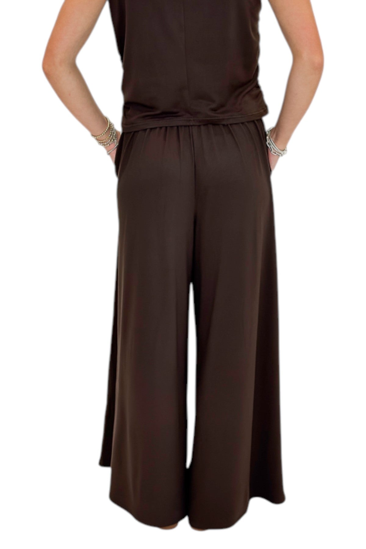 Back view of woman wearing Swagger Boutiqueβs Brown Pleated Wide Leg Pants with Brown Rouched Side Tank against white studio background.